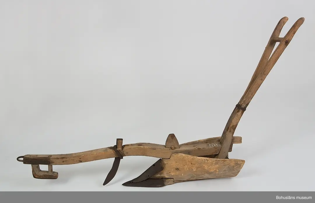 Träårder med smidd plogbill som kopplas till ett dragok. 
Dragårdret sammanhör med Drakok, UM027773

Ur handskrivna katalogen 1957-1958:
Årder att dragas för hand
L. c:a 152 cm. Järnbeslag. Dragträ l. m. kätting. Föremål. Järnet ngt rostigt. Träet maskätet.