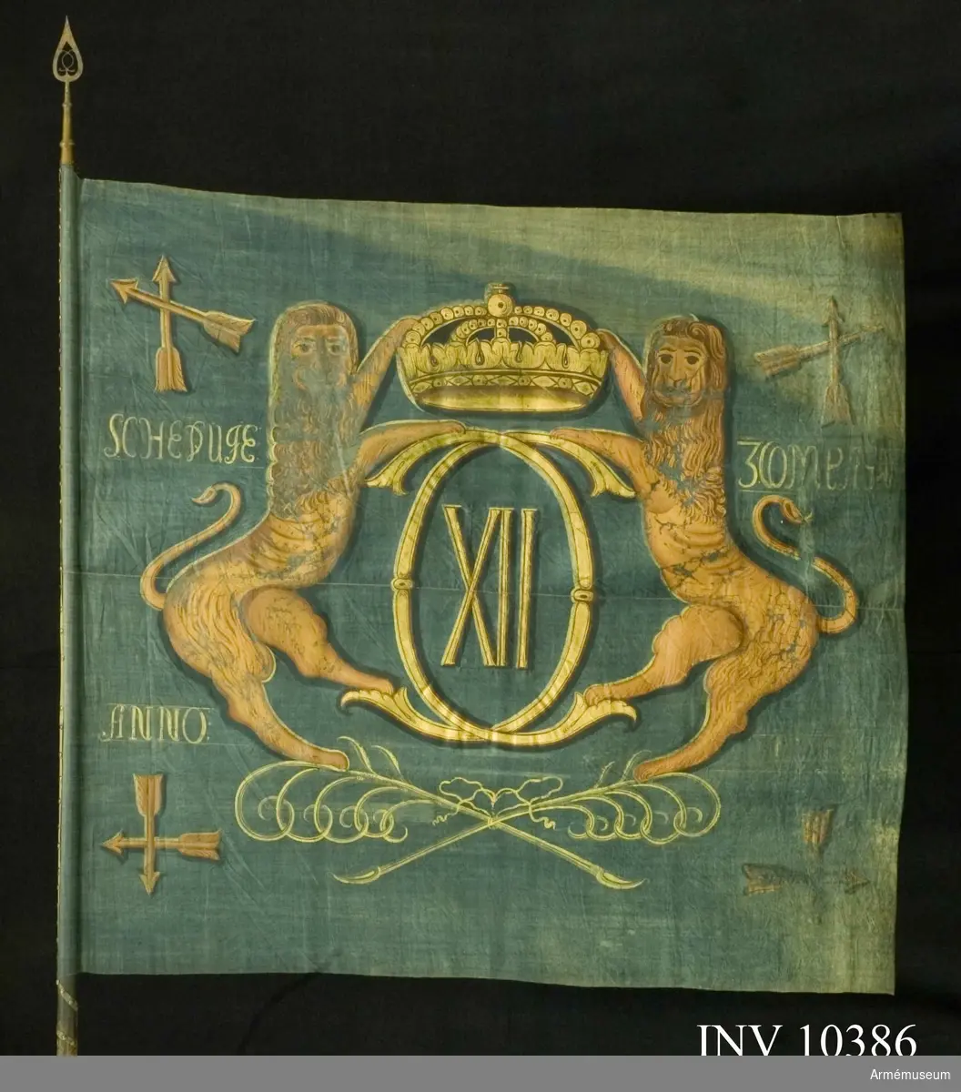 Grupp B I.
Fanduk av blå lärft, hopsydd av två våder, med målade emblem: Karl XII:s spegelmonogram av dubbelt C med XII därinom under sluten kunglig krona, hållet av två gulbruna lejon, som står på två korslagda och med bandrosett hopknutna palmkvistar i grönt. I vardera hörnet Dalarnas sköldemärke, två korslagda pilar inom korslagda palmkvistar, allt i gulbrunt och brunt.

Namnchiffret och kronan i guld, övriga emblem i gulbrunt och brunt. Fastspikad med blått linneband och mässingsspikar. Bandet lindat sex varv runt stången nedom duken. Stång av grönblåmålad furu. Spets av mässing i ett stycke, holken med  profilerade vulster. Bladet med Carl XII:s spegelmonogram i  genombrutet arbete, dess längd 29 cm.