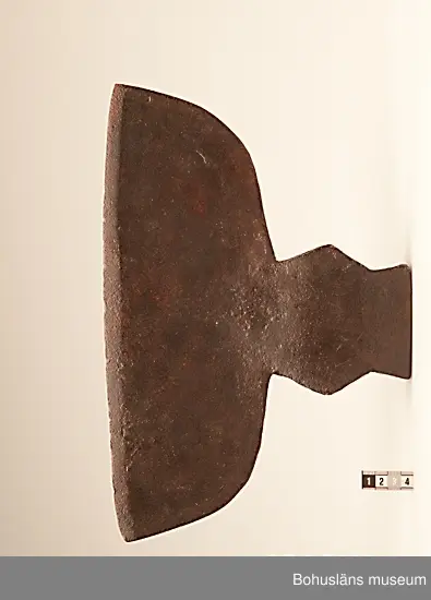 Handsmidd enkeleggad bred yxa med romboid holk med rektanguulärt uttag för skaft. Yxskaft saknas.
Viss gravrost.
Förvärvad 1952 från Johannes Olsson, Stillingön, Orust och då med uppgiften att yxan använts som bödelsyxa.

Svårbedömd tillverkningstid.

Ur handskrivna katalogen 1957-1958:
Bödelsyxa
L. 36,5. Br 24,5. Föremålet helt. Något rostat.