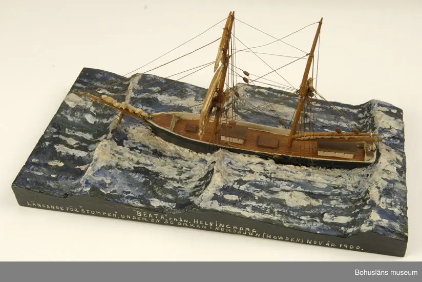 Bramsegelskonaren Beata från Helsingborg, 
Tillverkad av kapten John Emil Olsson (1880-1950), Fiskebäckskil på Skaftö i Lysekils kommun på 1940-talet.
Trä, metall, lintråd, tyg, gips.
Höjd 20 cm, längd 32 cm, B 9 cm. Platta längd 42 cm och bredd 20,5 cm. Okänd skala.
Vattenlinjemodell med två master, grönmålat skrov, röd bottenfärg, övriga detaljer vitmålade eller lackade. Stående och löpande rigg med utskurna block. Undre märssegel av snidat trä, revade segel av gasväv samt med däckshus, lastluckor och ratt. Monterad på utskuren platta med modellerad och målad gipssjö.
På plattans långsida har kapten Olsson textat med vita tryckbokstäver:
"BEATA". FRÅN HELSINGBORG 
LÄNSANDE FÖR "STOMPEN", UNDER EN SO ORKAN I NORDSJÖN (HOWDEN) NOV ÅR 1900.

Modellen föreställer hur fartyget förlorar däcklasten överbord i en orkan i Nordsjön.
I Sjöfartsbok för John Emil Olsson utfärdad vid Uddevalla Sjömanshus framgår att han var mönstrad som matros på Beata som gjorde fyra resor från Hasle på Bornholm till England via Norrland under befälhavare N. P Nilsson den 16 mars - 11 december 1901.

Definitioner:
Seglet på näst understa rån på råriggad mast kallas undermärssegel eller stump. 
Vid hårt väder beslogs fartygets alla segel utom undermärsen och man seglade "för bara stumpen". 
Blev vädret värre fick man försöka rida ut stormen och ligga bi för sviktade stumpar. Då revades halva stumpen så att bara en trekant blev kvar på rånockens ena sida.

John Emil Olsson var mönstrad på Beata  med hemmahamn Helsingborg som matros  16 mars t o m 11 december 1901 för resa  Hasle - England via Norrland (fyra resor) . 
Ur handskrivna katalogen 1957-1958:
"Beata"
Modell på platta. L. (från för till akter) 25. Föremålet helt.
Från kapten Olssons saml., Fiskebäckskil.

För ytterligare information om John Emil Olsson och förvärvet, se UM005807.

Föremålet presenterat på Bohusläns museums hemsida år 2009 - 2013, webbutställning "John Emil Olsson Fiskebäckskils sjöfartsmuseum".