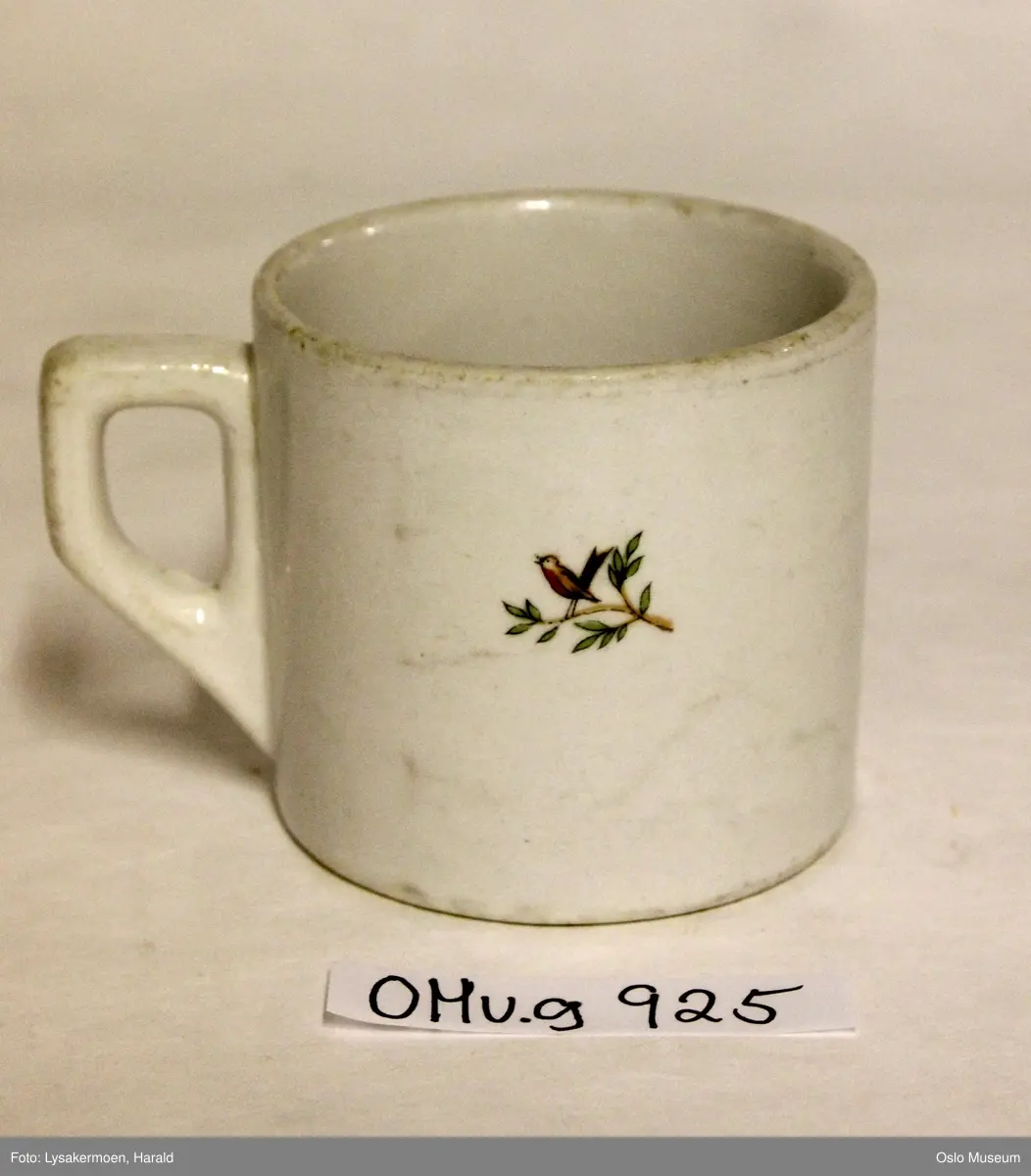 Gutt og jente sitter rygg mot rygg, i blomstereng med fugl som synger fra kvist. Han spiller fløyte og hun synger. Han har grønn hatt, lys brune (gule) bukser og brun overdel, hun har rød kyse, rødt skjørt med hvite prikker og blå kortermet overdel / bluse.