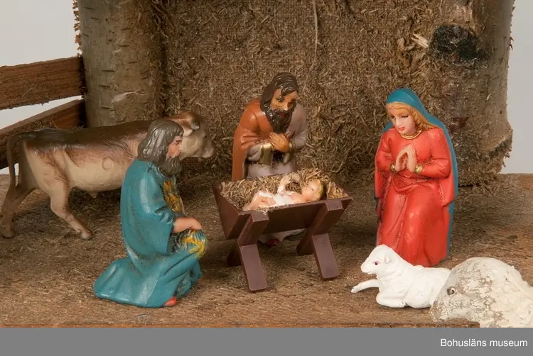 Stall med halmtak, trästolpar samt golv och vägg av masonite. Märkt UM19818:1
18 st figurer tillhör julkrubban. De är märkta UM19818:2.
Krubba, Jesusbarnet, Maria, Josef, en herde, de tre vise männen, en åsna, en oxe, tre liggande får, fem stående får varav ett betydligt större.
En av de tre vise männen märkt: Germany
Elastolin brukar denna typ av plastisk massa benämnas - egentligen ett  tyskt inregistrerat varumärke på en kompositmassa.
