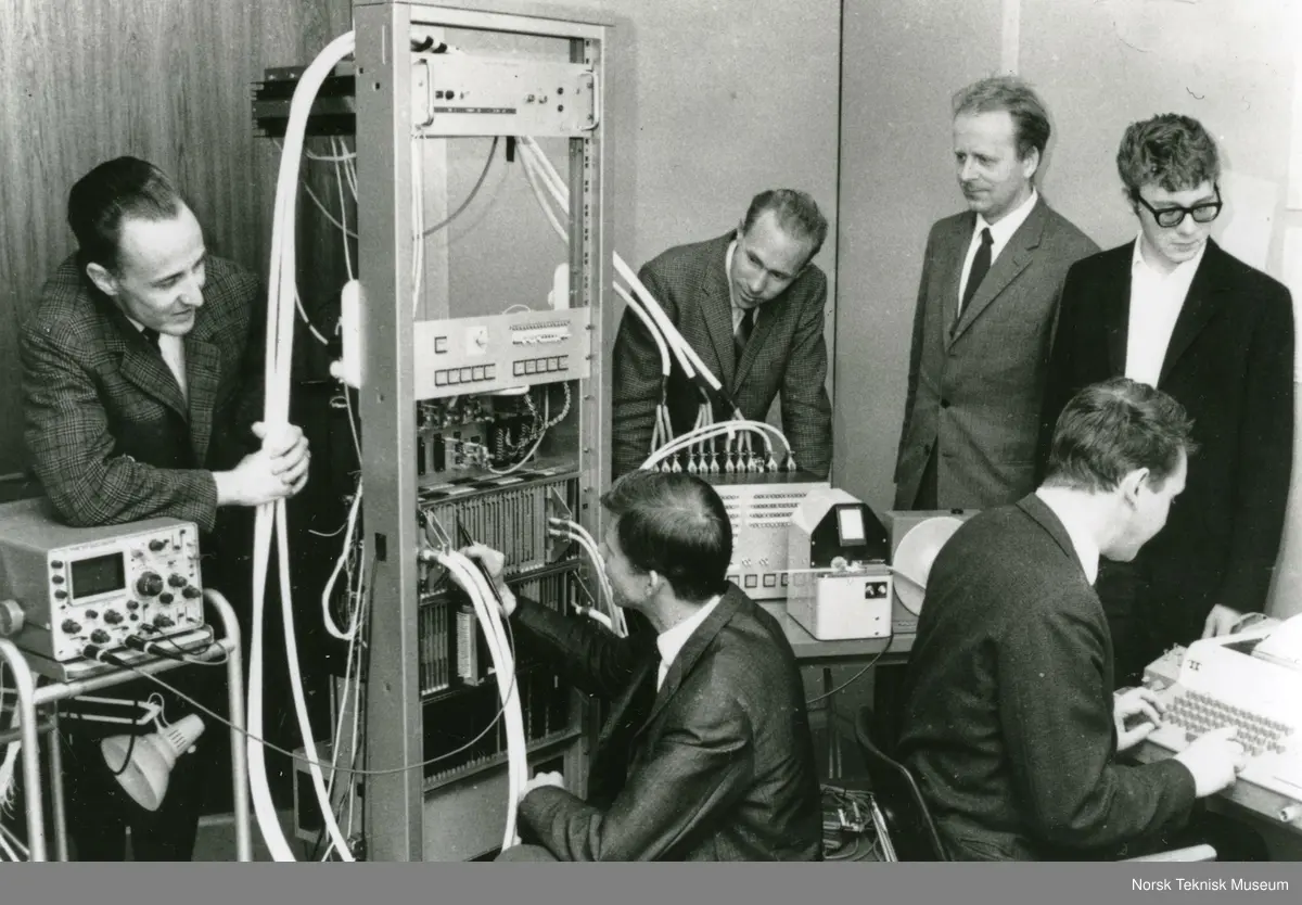 Norsk Data: Seks menn, deriblant Lars Monrad Krohn og Rolf Skår, samlet rundt en Nord-1 minidatamaskin fra 1968, en tredjegenerasjon maskin basert på integrerte kretser (IC), Nord-1 maskinen ble benyttet til tekniske og administrative oppgaver. Fra venstre bak Per Bjørge, Ove Raffelsen, Lars Monrad Krohn, Tom Weum, fra venstre foran Tor Monsen, Rolf Skår