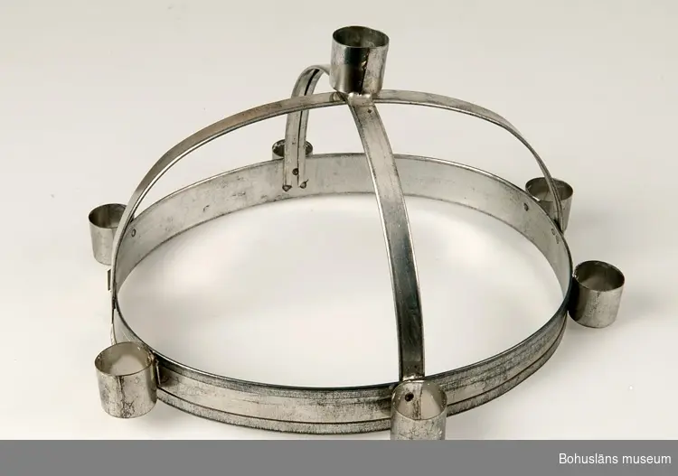 Luciakronan ställbar med oval nederdel med sex nitade ljushållare, från nederdelen utgår två tvärgående band i bågform. Där banden möts finns en sjunde fastlödd ljushållare.