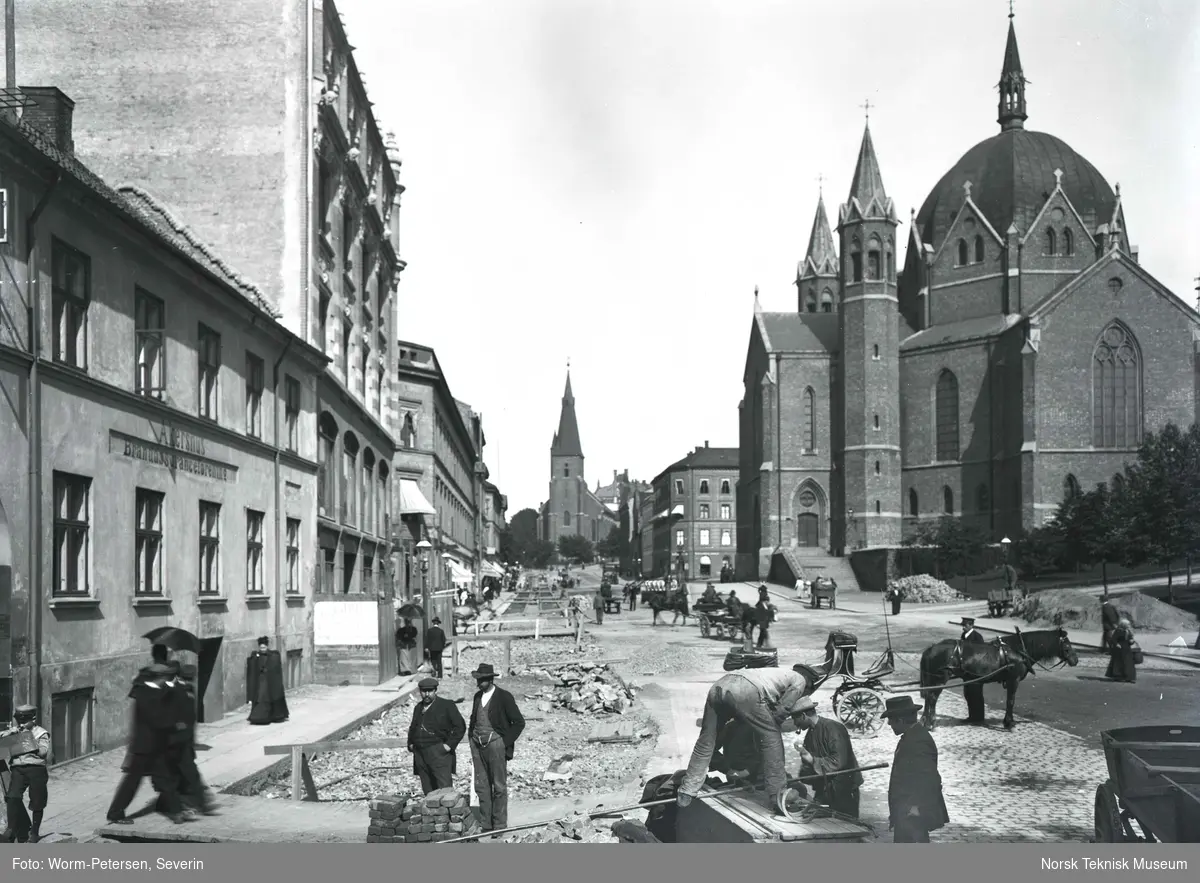 Legging av trikkeskinner i Akersgata i 1899. Bildet er tatt under arbeidet med ny sporvei fra Akersgata 18 der leseselskapet Athenæum lå, til St.Hanshaugen. Trefoldighetskirken ligger til høyre og St.Olavs kirke i bakgrunnen.