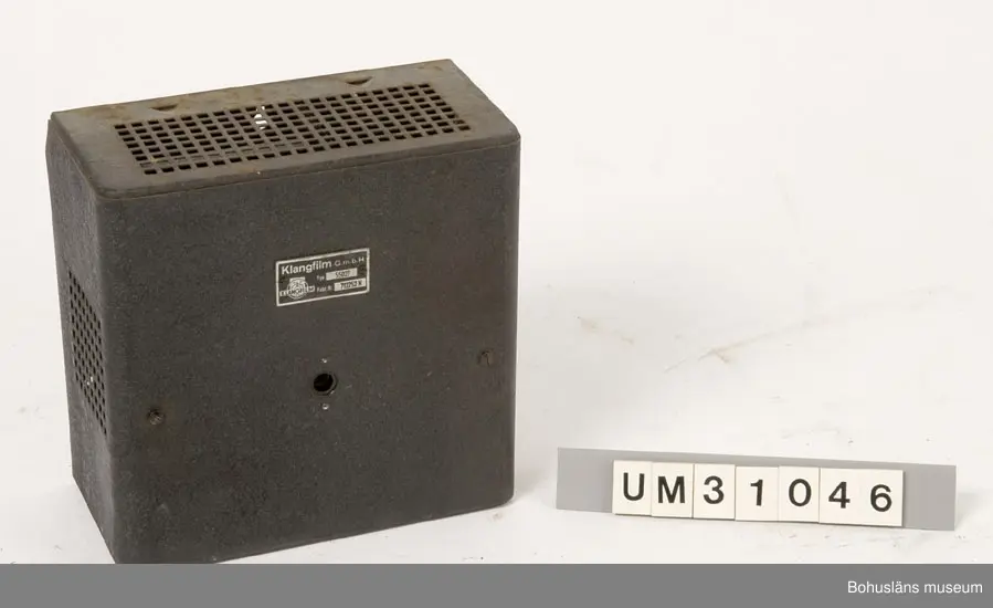 Elskåp av svart brännlackerad plåt för väggmontering med oklar användning, kanske  till ljudanläggningen. Kan det vara förstärkare till en högtalare?

Rektangulär låda märkt med metallskylt:
KLANGFILM
G. m. b. H.
Runt hål för liten kontakt placerad mitt fram. 

Skåpet har använts tillsammans med  projektor UM31031. 

Projektorn är tillverkad av AEG på 1920-talet och har använts i Folkets Hus i Sjöbol vid Lysekil.

Till projektorn hör en lång rad delar och olika tillbehör, UM31031 - UM31062.

För ytterligare upplysningar om filmprojektorn, dess olika delar och användning, se UM31031.