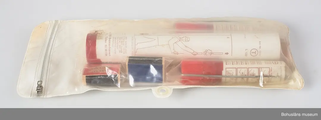 Plastförpackning med nödsignaler innehållande en större fallskärmssignal och två mindre handfacklor och två askar med stormtändstickor, allt i separata plastförpackningar. Försluts med dragkedja av plast. 
På baksidan tryckt text:
KEEP DRY
It is essential that these signals be inspected frequently and
kept dry. These packs afford good protection but should not
be expected to withstand prolonged immersion in water."
På föremålen beskrivs användnng i bild och text.