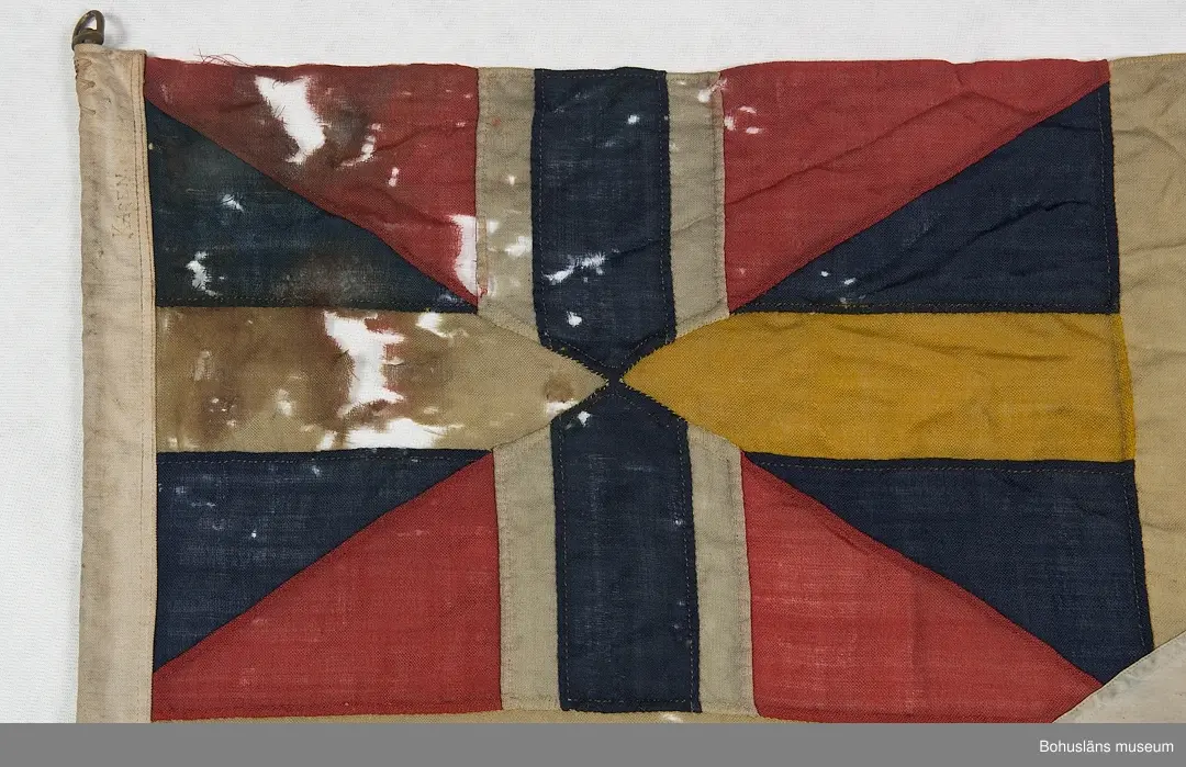 Segelsällskapet Vikens flagga, SS Viken. 
Svensk tvåtungad  flagga med parti "Silllsallaten", svensknorska unionsflaggan i övre hörnet samt infällt handmålat rombiskt emblem placerat mitt i det gula korset. På emblemet är målat ett vikingaskepp. 
Märkt "KASEN" med svart märkbläck. Hand- och maskinsömnad.
Skador. Eventuellt har flaggans form ändrats.