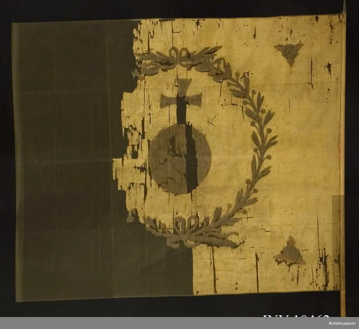 Fanduk av vitgul (röd) taft med målade emblem: Upplands sköldemärke: ett riksäpple i brunt, svart och gult, allt inom en lagerkrans av två kvistar med tätt ställda blad, nedtill hopknutna med bandrosett. I hörnen brinnande fyrkulor i svart och rött. Ursprungligen fastspikad med sidenband och kupiga mässingstift, nu fastspikad med några spikar och f ö fastsydd. Stång av brunpatinerad furu. Spets av järn, troligen sekundär, holken enkel, bladet massivt.
