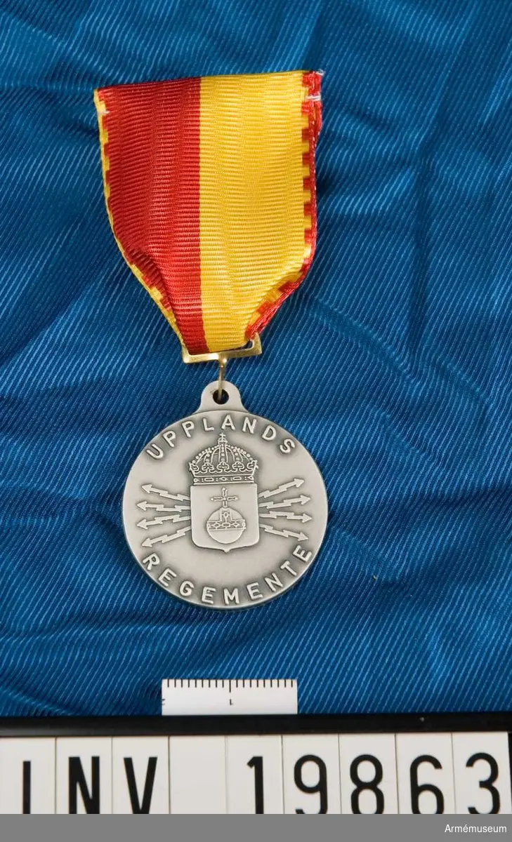 Medaljen är rund. I skölden ett riksäpple. Skölden krönt med en kunglig krona och lagd över ett knippe blixtar. En öppen lagerkrans. Inskription: Upplands regemente. Band kluvet i rött och gult samt med stickade kanter i motstående färg. Medaljen förvaras i ask.