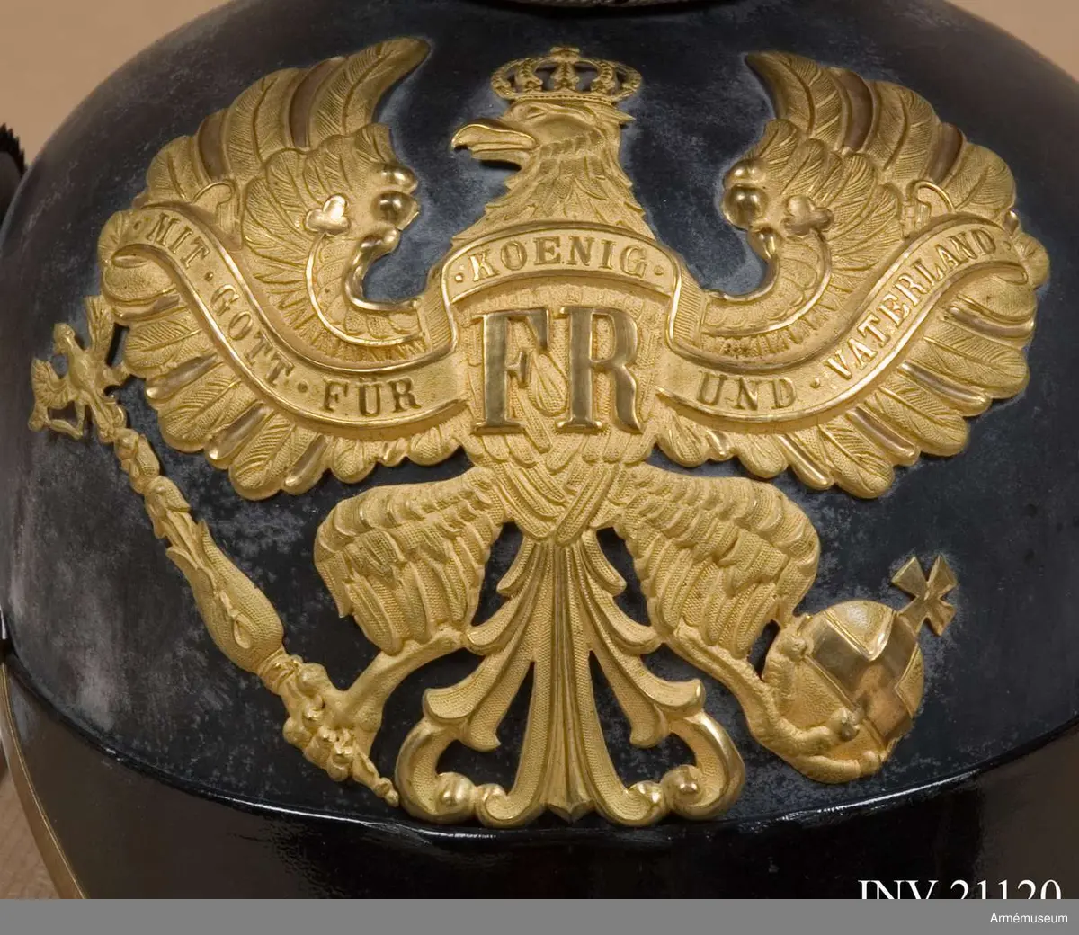 Vapenplåt på mössans framsida heraldiskt preussiskt vapen för linjetrupper med svärd och spira. 
På örnens bröst finns två bokstäver: "FR"- "Fredricus Rex" efter dagorder 14 mars 1844. Jämte devis "Mitt got für könig und Vaterland" efter dagorder 20 juli 1860. 
Övre delen består av fyrkantig lock längd och bredd, 14,5 cm med hake ovanpå för mössnören. I mitten på V sida finns ett hål för att fästa nationalfältmärket och tagelplym.