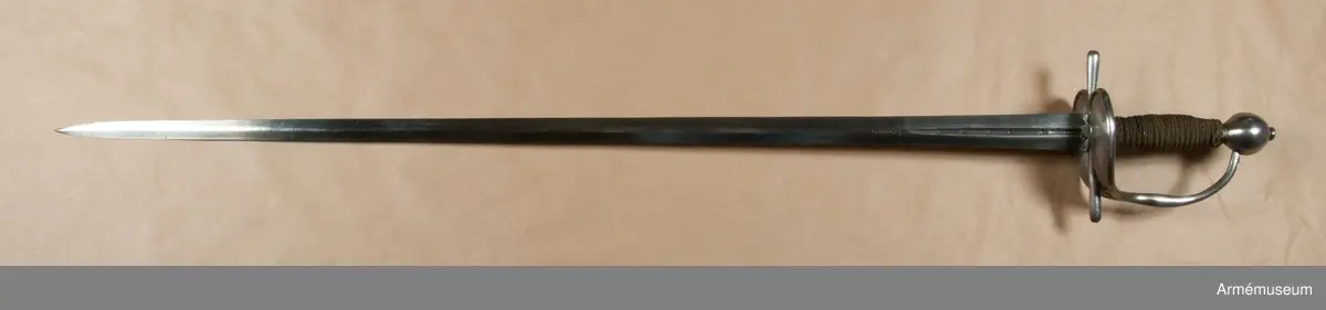 Klingan är tveeggad med flata åsar. Upptill på var sida har den en blodrand, som på yttersidan är 16,5 cm lång. Under den nedra ändan på varje blodrand finnes ett av prickar bestående onament.

Fästet är av polerat järn och av drabanttyp. Knappen är svagt ellipsiodisk med rygg fram och bak. Diam. sidled är 3,95 cm, men över ryggarna 4,15 cm. Höjden är 4,3 cm. Nitknappen är låg och närmast cylindrisk. Halsen är ävenledes låg med konisk. Höjden av hals, knapp och nitknapp är sammanlagt 5,25 cm. 
Kaveln är spolformig med flat rand fram och bak, men sidorna är avrundade. Upp- och nedtill omgives den av en ringliknande, platt flätning, "krans", av rätt varierande bredd, i huvudsaken dock 0,7 cm, vilken flätning består av mässingstråd, men är hopsnodd av två parter. I övrigt är kaveln lindad med 4 mässingstrådar, av vilka två är rätt grova, den ena höger- den andra vänstersnodd, men de båda övriga rätt fina.
Parerstången är nästan rak och blir mot ändarna litet bredare. Den främre änden är avrundad, men den bakre har mer tvär avslutning. Armarna ha spetsovalt tvärsnitt. Den största bredden är för den främre armen 1,1 cm, men för den bakre 1,25 cm. Den största tjockleken är för bägge armarna 0,85 cm. Avståndet mellan den främre eggen och parerstångens främre ändan är 6,8 cm, men mellan den bakre eggen och den bakre änden 5,9 cm. 
Parerplåten är hjärtformig och har förhöjda kanter, vilka sistnämda egentligen bestå av spänger, en på var sida, vilka från parerstångens bakre arm gå till handbygelns nedre del. Tomrummen mellan spängerna och parerstången, resp. handbygelns nedre del, ha utfyllts med ett par kupiga plåtar, som faslötts med mässing. Parerplåten är något större på ytter- än på insidan. Avståndet mellan klingans mitt och parerplåtens kant är på det förstnämda stället 4,6 cm, men på det sistnämda 4,5 cm. 
Handbygeln utgår från korset, har spetsovalt tvärsnitt och den största bredden litet ovanför parerplåtens spets. Dess övre ända är instucken i ett hål i knappen. På handbygelns innersida nära övre ändan är bokstäverna AD inslagna. Tumbygel finnes icke.
