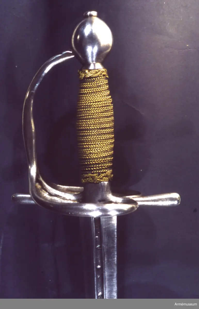 Klingan är tveeggad med flata åsar. Upptill på var sida har den en blodrand, som på yttersidan är 16,5 cm lång. Under den nedra ändan på varje blodrand finnes ett av prickar bestående onament.

Fästet är av polerat järn och av drabanttyp. Knappen är svagt ellipsiodisk med rygg fram och bak. Diam. sidled är 3,95 cm, men över ryggarna 4,15 cm. Höjden är 4,3 cm. Nitknappen är låg och närmast cylindrisk. Halsen är ävenledes låg med konisk. Höjden av hals, knapp och nitknapp är sammanlagt 5,25 cm. 
Kaveln är spolformig med flat rand fram och bak, men sidorna är avrundade. Upp- och nedtill omgives den av en ringliknande, platt flätning, "krans", av rätt varierande bredd, i huvudsaken dock 0,7 cm, vilken flätning består av mässingstråd, men är hopsnodd av två parter. I övrigt är kaveln lindad med 4 mässingstrådar, av vilka två är rätt grova, den ena höger- den andra vänstersnodd, men de båda övriga rätt fina.
Parerstången är nästan rak och blir mot ändarna litet bredare. Den främre änden är avrundad, men den bakre har mer tvär avslutning. Armarna ha spetsovalt tvärsnitt. Den största bredden är för den främre armen 1,1 cm, men för den bakre 1,25 cm. Den största tjockleken är för bägge armarna 0,85 cm. Avståndet mellan den främre eggen och parerstångens främre ändan är 6,8 cm, men mellan den bakre eggen och den bakre änden 5,9 cm. 
Parerplåten är hjärtformig och har förhöjda kanter, vilka sistnämda egentligen bestå av spänger, en på var sida, vilka från parerstångens bakre arm gå till handbygelns nedre del. Tomrummen mellan spängerna och parerstången, resp. handbygelns nedre del, ha utfyllts med ett par kupiga plåtar, som faslötts med mässing. Parerplåten är något större på ytter- än på insidan. Avståndet mellan klingans mitt och parerplåtens kant är på det förstnämda stället 4,6 cm, men på det sistnämda 4,5 cm. 
Handbygeln utgår från korset, har spetsovalt tvärsnitt och den största bredden litet ovanför parerplåtens spets. Dess övre ända är instucken i ett hål i knappen. På handbygelns innersida nära övre ändan är bokstäverna AD inslagna. Tumbygel finnes icke.