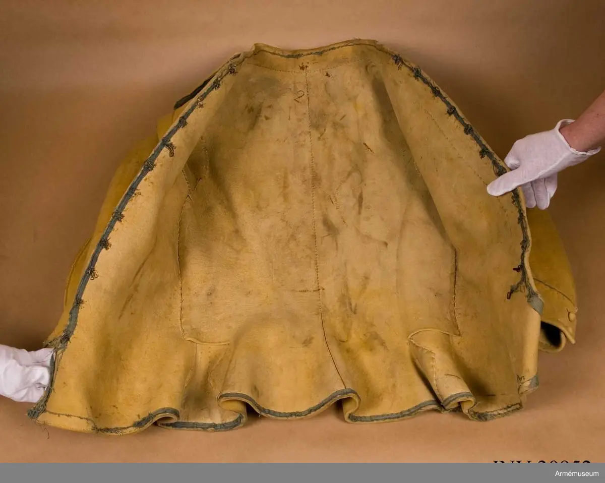 Kyller av gul älghud med blå linneband som kantning på insidan. Lätt utsvängt nertill med litet skört bak. Uppvik framtill, axelkarmar och låg krage.  Kragens linneband är i dag i upplösning och bara några trådar finns kvar.
Helt framtycke, och delat bakstycke samt två separata sidstycken. Sidsöm under ärmen.
Formade tvåsömsärmar med ärmuppslag. Ärmuppslagen har blå passpoal och sprund som knäpps med 3 koniska knappar klädda med sämskskinn i samma färg. Ett fjärde knapphål som är igensytt talar om att plagget blivit omsytt vid något tillfälle. En rad hål efter stygn på insidan av höger framstycke visar att plagget har haft en knappstolpe/underlott.
Axelklaffar fodrade med blått linne som knäpps vid kragen med samma knappar som ovan.
Plagget knäpps kant i kant mitt fram med 12 stycken hyskor och hakar av metall. Alla sömmar är sydda med oblekt lintråd.
Märkt inuti ryggen med "N 2".