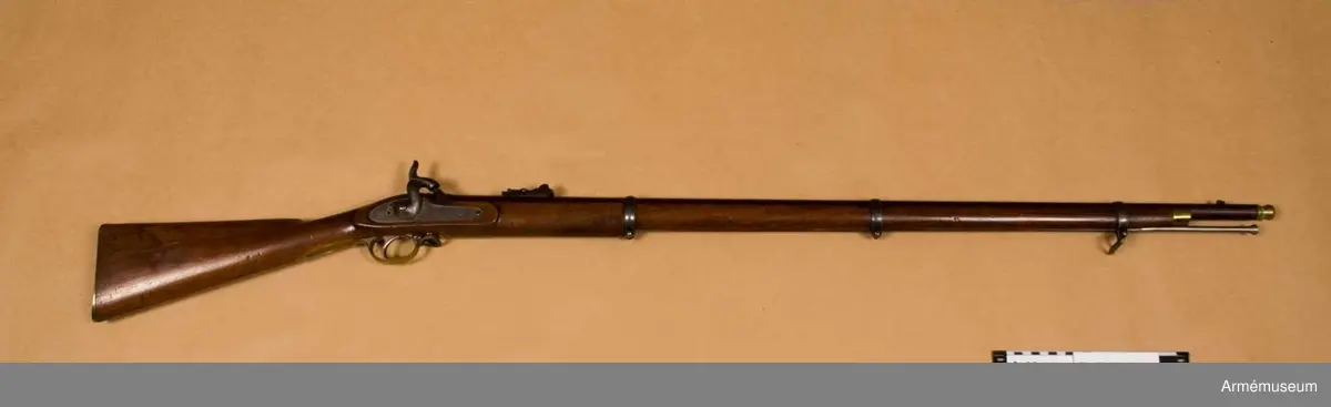 Grupp E II.
Gevär med slaglås.
Antal räfflor: 3. Räffelstigning: ett halvt varv på piplängden. Kulvikt: 34 g. Krutladdningens vikt: 4 g. Pipan är brungjord och rund, men har baktill på översidan en 3,5 cm lång avplattning. Snäckan är rätt liten. En fyrkantig kombinerad bajonett- och kornklack sitter 3,3 cm bakom mynningen och på översidan av denna klack sitter det orörliga kornet. Ramtrappsiktets fot sitter 8,9 cm framför pipans bakre ände. Siktet har gradering för avstånd mellan 100 och 900 yards= resp 90 och 810 m. På pipans översida står PRITCHETT 7 POULTRY LONDON och på vänstra sidan är två Londonstämlar inslagna.

På det gråhärdade, framåtliggande kedjelåset är hanen och låsblecket längs kanterna prydda med ett par ingraverade ränder. stocken är av valnöt. Framstocken har en avsats för vart och ett av de tre banden. Piprännan är utvidgad alldeles bakom näsblecket. Bakplåten och varbygeln är av mässing. Den förstnämnde har en ganska lång, smal flik, som går in över kolvryggen och som längst fram är fäst med en skruv, under det att två skruvar sitter i bakplåten. Geväret har egentligen ej sidbleck, utan kring vart och ett av de bägge hålen för låsskruvarna finns en smal, ringliknande mässingsskoning, från vilken en kort arm går framåt och en annan bakåt. De tre banden är av gråhärdat järn och ha på undersidan öron, som förenas genom en skruv. Det främsta bandet ligger 8 cm bakom stockens framände och skruven på detta band fasthåller den främre rembygeln. Näsblecket är av mässing, och fasthålles av en underifrån kommande skruv. Den bakre rembygeln är fäst i varbygelns främre del.

Laddstocken är av stål och har skålformigt huvud. Omkring 12 cm från framänden har laddstocken en ungefär 2,5 cm lång förtjockning, som passar i laddstocksrännans ovan omtalade utvidgning. I smaländen är laddstocken gängad på en längd av 0,8 cm. Litet bakom huvudet finns fyra nästan utslipade bokstäver (R & K?).

Om den till detta gevär använda ammunitionen, se AM 6117-6120. Uppgiften om reffelstigningen har hämtats ur Jochnick, Handgevärslära, Stockholm 1863 paragraf 60. Geväret kallas vanligen Enfield- pritchetgeväret, då det konstruerades av gevärsfabrikanten Pritchett och antogs av den i Enfield församlade gevärskommiten. Av allt att döma har alltså den ovan beskrivna gevär tillverkats av konstruktören.