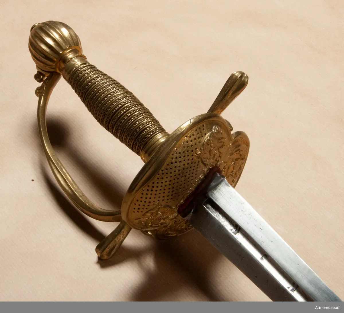 Klingans bredd upptill är 30 mm. Parerstångens längd är 145  mm. Klingan är tveeggad med flata åsar samt har på ömse sidor en blodrand, vid vars slut klingan prydes av ett ornament. Fästet är ett "franskt fäste" av ursprungligen förgylld mässing. Knappen är oval, upp- och nedtill tillplattad och på sidorna prydd med räfflor. Nitknappen är låg, runt sidorna krusad, nedåt instrypt och försedd med en stor, rund fot. Halsen är instrypt och kring sin nedre kant krusad. En rand eller snarare avsats markerar gränsen mellan knappen och nitknappen samt mellan knappen och halsen, och en sådan går även runt halsens nedre del. Kaveln är spolformig med ovalt tvärsnitt och lindad med tre mässingstrådar, av vilka en är slät, men de båda andra  är sammansnodda av två parter; den ena tråden är höger-, den  andra vänstersnodd. Upp- och nedtill omges kaveln av ett omkring 8 mm brett, med tre ränder prytt band av förgyllt  mässingsbleck. Parerstången har närmast sexkantigt tvärsnitt, blir tjockare mot ändarna och pryds där, i likhet med handbygelns mitt, av sex räfflor. Parerplåten är på mitten prydd med ciselerade ornament, men är i övrigt fint prickig samt genombruten av runda hål.