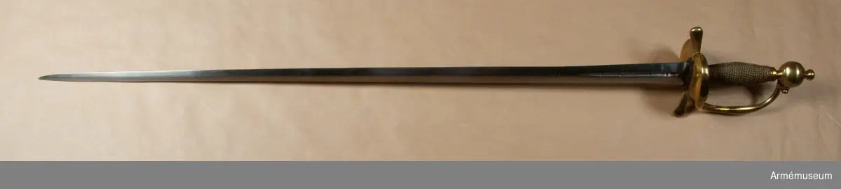 Klingan är tveeggad. Upptill på bägge sidor har den en omkring 140 mm lång blodrand. På yttersidan sitter dessutom en P-stämpel. Vid varje blodrands nedre ände finns ett delvis bortslipat, av prickar bestående ornament. Klingan är starkt avslipad, så att åsarna nedanför blodrandens slut nära nog förvandlats till ryggar. Fästet är av mässing och av drabanttyp. Knappen har formen av ett hoptryckt klot samt har rygg på fram- och baksidan. Knappens diameter är i sidled 37,5 mm, men över ryggarna 40,5 mm. Höjden är 33 mm. Upptill har knappen en stor nitknapp, som är instrypt. Nitknappens höjd är 16 mm, och diametern är 16 mm. Den har en spetsoval fot, som är 22 mm lång och 17 mm bred. Halsen är instrypt och 11 mm hög. Gränsen mellan nitknappen och knappen samt mellan knappen och halsen markeras genom en rand eller avsats. En dylik går även kring halsens nedre del. Knappen är rätt illa gjuten. Kaveln är spolformig, har fram och bak en flat rand, men sidorna är kullriga. Den har upp- och nedtill ett omkring 8 mm brett ringliknande beslag av mässingsbleck, varje beslag är prytt med två ränder samt är i övrigt lindat med två mässingstrådar, en grövre och en finare, vardera hopsnodd av två parter. Den ena tråden är höger-, den andra vänstersnodd. Parerstångens armar har spetsovalt tvärsnitt, är nedåtböjda samt blir mot de lindrigt avrundade ändarna tjockare och betydligt bredare. Den största tjockleken är för den främre armen 18,5 mm och för den bakre 18 mm. Avståndet mellan den främre eggen och  parerstångens framände är 54,5 mm. Mellan den bakre eggen och  bakänden är avståndet också 54,5 mm. Avståndet mellan klingans mitt och parerplåtens ytterkant är 52 mm, men mellan klingans  mitt och innerkanten 46 mm. Handbygeln är tjockast och bredast ungefär på mitten. Den har spetsovalt tvärsnitt och dess övre ände är fäst med en skruv vid knappen. På yttersidan av parerstångens främre arm finns en stämpel med bokstäver, sannolikt N. S.