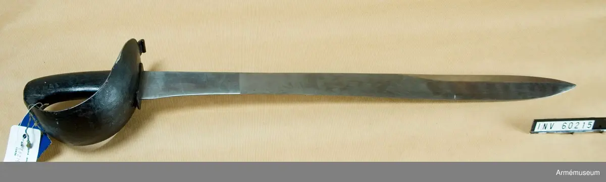 Grupp D II.  
Klingan är av samma typ som på AM 60213 och av Hafströms  konstruktion. Upptill är den 43 mm bred, men 120 mm längre ned  är bredden blott 33 mm. Sedan tilltar den så småningom, så att  450 mm, längre ned är den 42 mm, varefter den åter avtar mot  udden. 250 mm ovanför udden får även ryggsidan egg, som  fortsätter till udden.Tången är bred och upptill framåtböjd. Kaveln bildas av ett par svartmålade träskenor, vilkas hålls fast vid tången genom tre nitar. Parerplåten är av svärtat järn, rätt stor, något uppböjd samt på yttersidan betydligt större än på innersidan. Baktill  utgår från parerstången en kort, rektangulär, baktill nedböjd  och med förstärkt bakre kant försedd flik. Framåt blir  parerplåten smalare samt tjänstgör som handbygel.Längst upp ligger dess övre ände ovanpå kavelns övre ände och fasthålls där genom att tången, som går upp genom ett hål på handbygeln är nitad på översidan