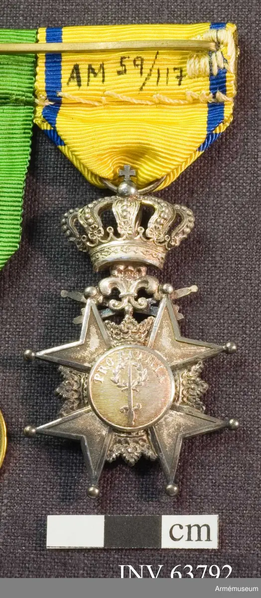 Grupp M II.
Svärdsmannatecken med band tilldelat styckjunkaren Georg Wilhelm Wessman.  Ett snedställt johannitkors av silver. Åtta uddar, var och en slutande i en kula. Mellan korsarmarna öppna kronor. På åtsidan har tecknet en blå, emaljerad glob i korstets mitt med ett stolpvis ställt svärd och tre öppna kronor ställda två och en. Mellan korsets övre vänstra udd och övre högra störtande svärd. Frånsidans mittglob är av silver med ett stolpvis ställt svärd omlagt med två kvistar ovanför "PRO PATRIA". Tecknet hänger i en kunglig krona. Medaljband av ett 35 mm brett sidenripsband - gult med mörkblå kantrand. 