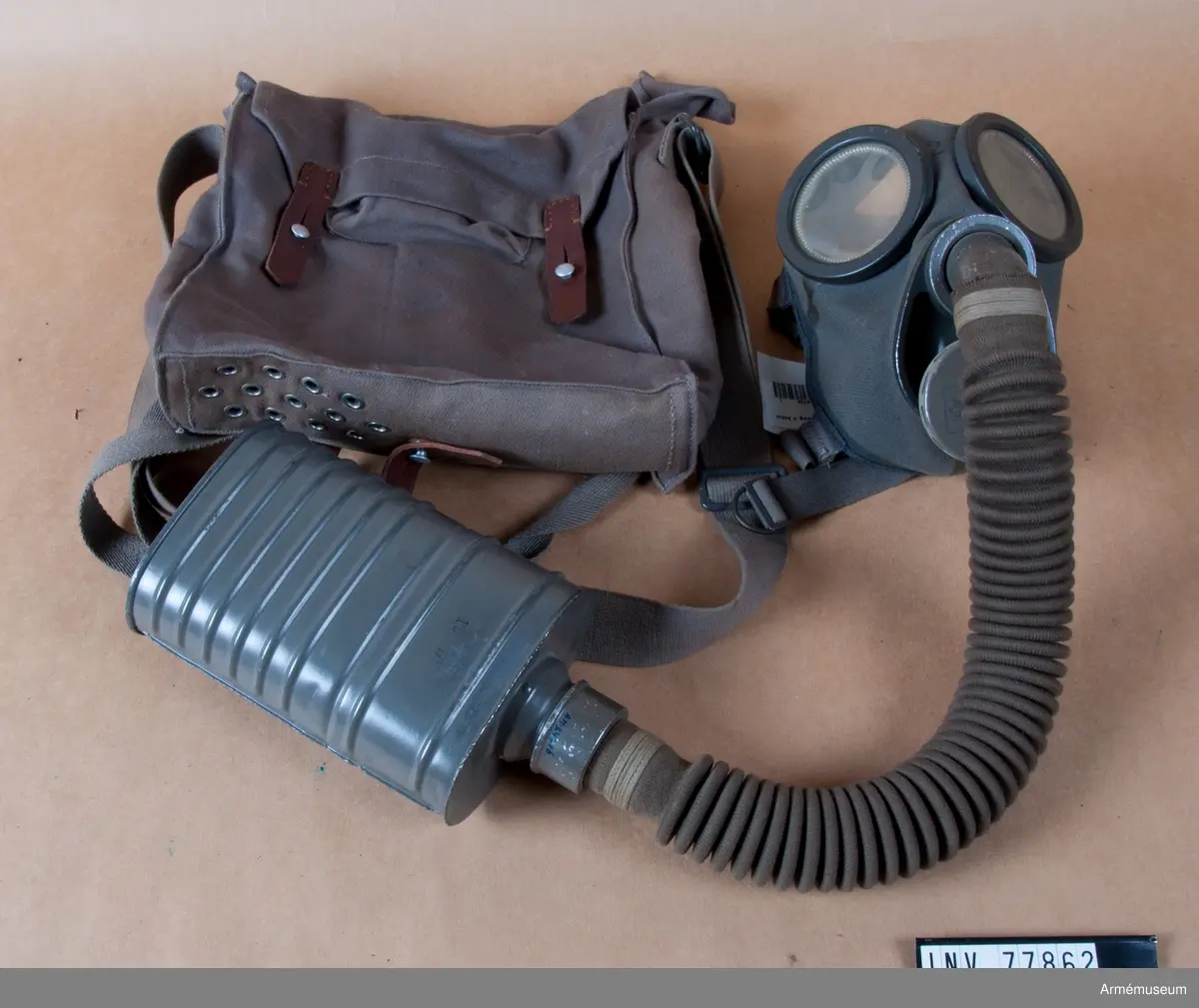 Grupp J.
Gasmask m/1931. Komplett med väska.
Består av ett ansiktsskydd m/1931, en ask för imskivor i reserv, en ask för ventilhus i reserv, en behållare m/1931, en slang, två ventilhus samt en väska m/1931.