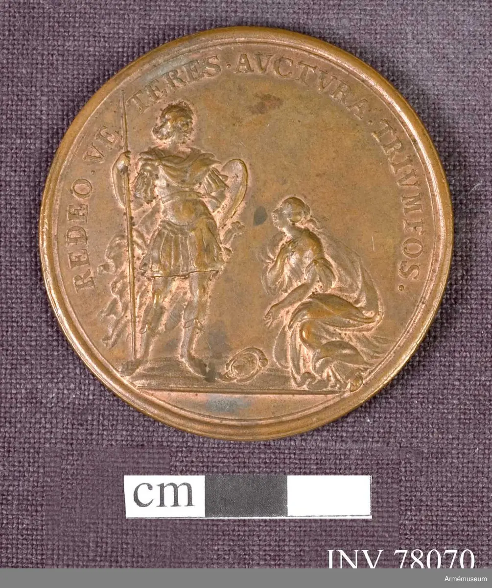 Grupp: M.
Åtsidan: HOC SOLO VI NDIGE TVTA. Konungens bröstbild åt höger, lagerkransad, i harnesk med fyrkantig öppning kring den bara halsen och mantelveck omlagda över axeln - På ett veck AK. 

Frånsidan: REDEO. VE TERES, AVCTVRA:TRIVMFOS. Konungen och en kvinna (Skåne) i antik dräkt, knäböjer med talande åtbörd framför konungen, som står klädd i antik rustning och mantel, med spjut, svärd och sköld. Konungens huvud bart med lagerkrans. (Jämför no. 6674) Framför kvinnan ligger en sköld med Skånes vapen, på vilken hon pekar.