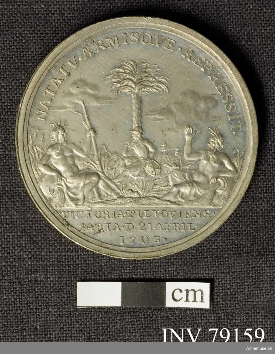Grupp: M.
Åtsidan: CAROLVS. XII. D.G. REX. SVECIAE. Bröstbild åt höger, lagerkransad i harnesk, som till största delen döljes av brämade mantelveck. Halsen bar med en veckad remsa över kanten av harnesket. Nedanför AK. 

Frånsidan: NATATV. ARMISQVE. REPRESSIT. En fånge, vilande armen på sachsiska skölden, sitter på marken, lutande sig mot stammen av ett palmträd. I förgrunden ligga två flodgudar med sina strömmande urnor, betecknande floderna Narew och Rosach. På fästet skyar. I avskärningen: VICTORIA PVLTOVIENS. PARTA. D 21 APRIL. 1703. 
 
Medaljen graverad av A Karlsten.