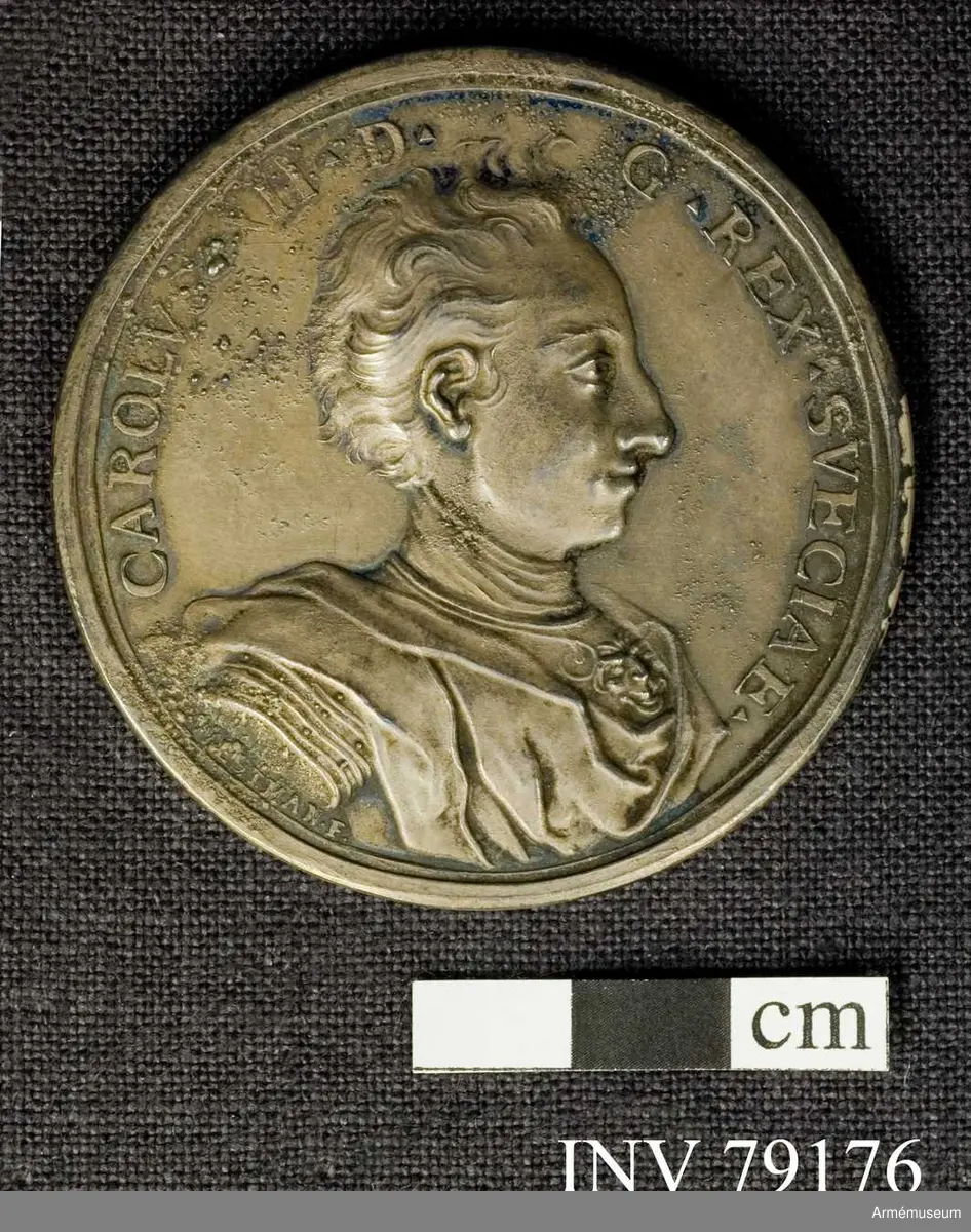 Grupp: M. 
Åtsidan: CAROLVS XII D G REX SVECIAE. Bröstbild åt höger i harnesk med lejonansikte på bröstet och släta mantelveck samt omlindad halsduk. Nedanför: B Westman F.

Frånsidan: LVSVS ET IVBILA SVECIS. Solguden på sin fyrspända vagn åker över stenbockens tecken i zodiaken. Nedanför sväva moln över ett landskap. I avskärningen: DANI ET SAXONES DEO VLTORE A STEN BOKKIO AD GADEBVSCH SVB SOLST BRVM A 1712 VICTI.