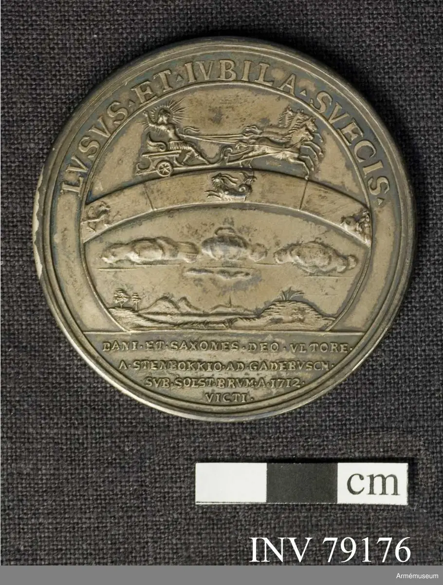 Grupp: M. 
Åtsidan: CAROLVS XII D G REX SVECIAE. Bröstbild åt höger i harnesk med lejonansikte på bröstet och släta mantelveck samt omlindad halsduk. Nedanför: B Westman F.

Frånsidan: LVSVS ET IVBILA SVECIS. Solguden på sin fyrspända vagn åker över stenbockens tecken i zodiaken. Nedanför sväva moln över ett landskap. I avskärningen: DANI ET SAXONES DEO VLTORE A STEN BOKKIO AD GADEBVSCH SVB SOLST BRVM A 1712 VICTI.