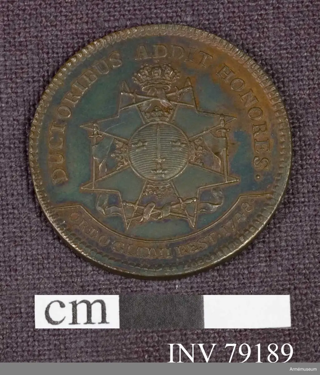 Grupp: M. 
Åtsidan: FRIDERICUS. D.G. REX SVECIAE. Bröstbild åt höger i harnesk med naglar i övra kanten, kronor på axelbetäckningen, halsduk och ordensband - Under armen ett svagt tecknat monogram, innehållande D.F. -Kanten på båda sidor strierad.

Frånsidan: DUCTORIBUS ADDIT HONORES. Svärdsordens storkors. I avskärningen: ORDO GLADII REST 1748. 

Graverad av D Fehrman.