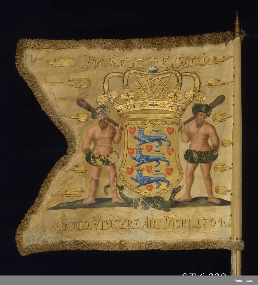 Tvåtungad dansk dragonfana, tillverkad av vit sidenatlas med målad dekor.

Fanan pryds av Danmarks riksvapen, en krönt sköld med tre blå lejon och nio röda hjärtan. I kronan finns spegelmonogrammet F4 (Fredrik IV) inflätat. På ömse sidor om vapnet står en vildman. Gyllene flammor täcker duken. På marken krälar en grön drake eller salamander. Upptill lyder devisen ”PRO REGE ET PATRIA” (För kung och fosterland), nedtill står det att läsa ”ANNO. VINCERE AUT MORI. 1704” (Segra eller dö) omgärdat av (år 1704).

Till Danmarks riksvapen har en grön drake eller salamander och gyllene flammor fogats. Salamandern och flammor förekommer på andra danska krigstroféer, både på fanor och på kanoner. Salamandern ansågs kunna släcka eld.