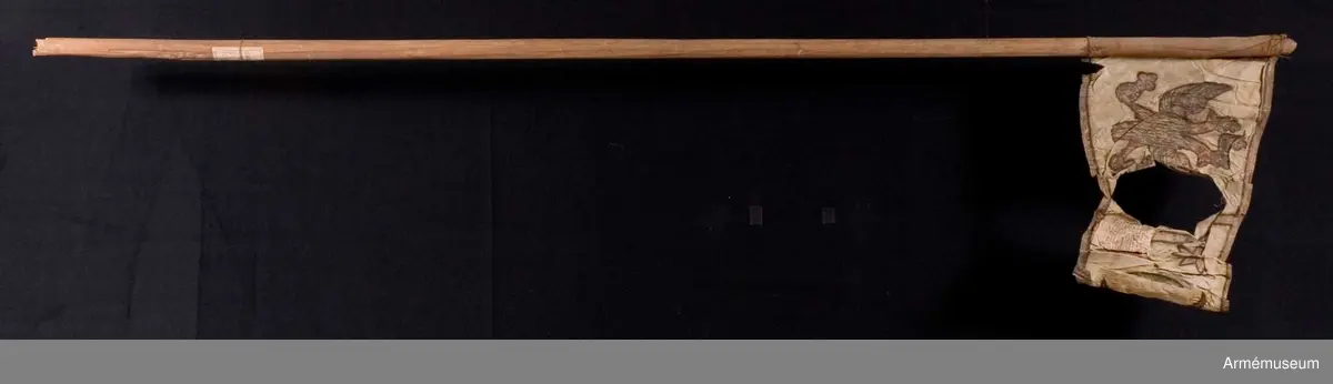 Duk av vit sidentaft och strumpa av rött linne. Motivet målat i guld- och silver samt rött och grönt bestående av en krönt örn, måne, sol och stjärnor, På duken en pappersetikett som anger att den tagits i slaget vid Saladen 1703.