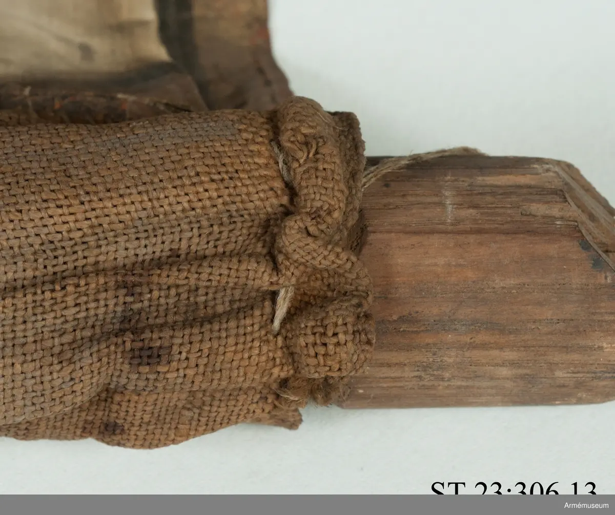 Duk av vit sidentaft och strumpa av rött linne. Motivet målat i guld- och silver samt rött och grönt bestående av en krönt örn, måne, sol och stjärnor, På duken en pappersetikett som anger att den tagits i slaget vid Saladen 1703.