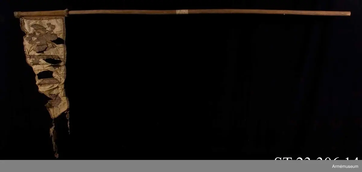 Duk av vit sidentaft och strumpa av rött linne försedd med frans vid öppningarna. Motivet målat i guld- och silver samt rött och grönt bestående av en krönt örn, måne, sol och stjärnor, På duken en pappersetikett som anger att den tagits i slaget vid Saladen 1703.