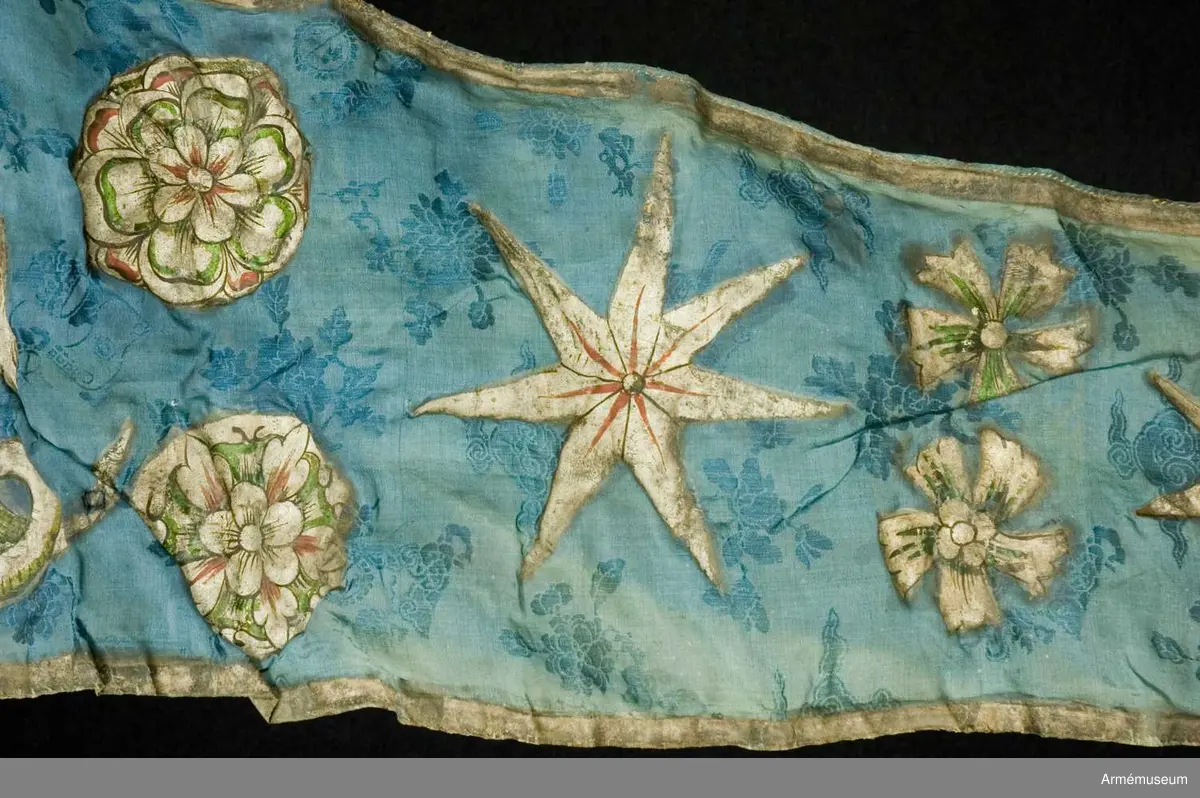 Entungad lansfana. Duk av blå kinesisk sidendamast med målad dekor. I 1703 års inventarium anges motivet vara St Göran men enligt den ryska inskriptionen är det Feodor Stratilat . Rosor och stjärnor av silver. Duken kantad med en silverbård. Strumpa av rött linne.