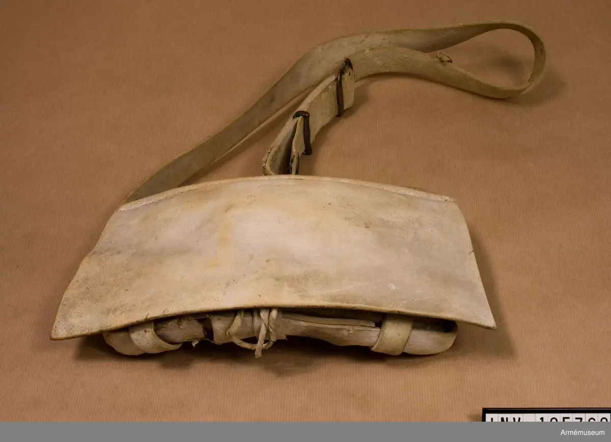 Patronväska av vitt sämskskinn med rem.
Inuti kartuchen finns en bleckplåtsinsats med rum för 12 patroner av ca 18 mm kaliber och plats för en liten oljeflaska. Under locket sitter även en extra ficka,