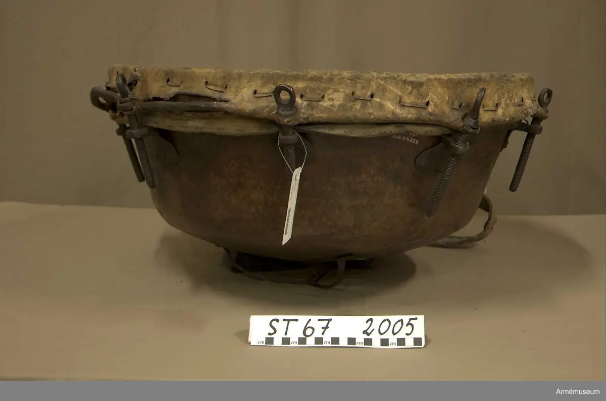 Kittel av koppar och skinn av kalv med fast spännring. Fot av järn fastnitad med kopparnit. Skruvar och skruvfästen av järn. Bärrem av kalvskinn i två lager med spänne av järn.