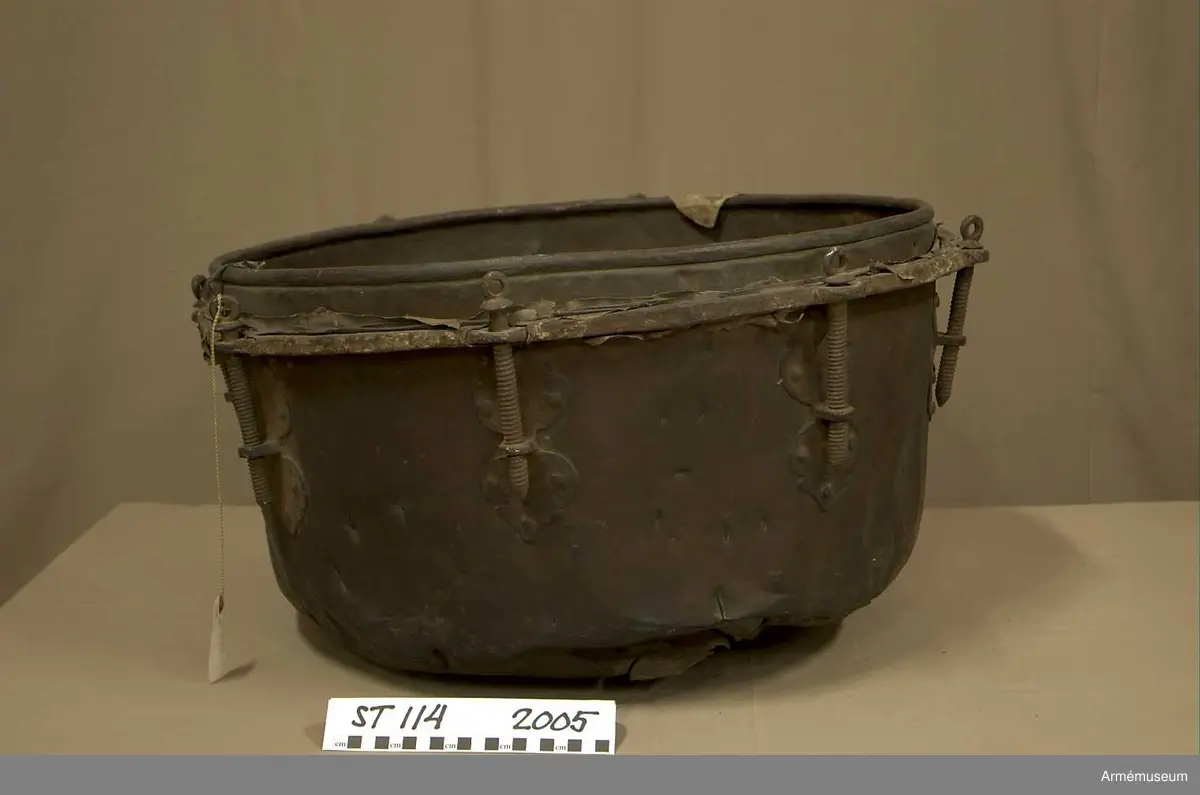 Tillstånd 2005:
Kittel: kraftigt bucklig och sprucken på flera ställen. En mängd stickmärken i storlek 1 cm. - 4 cm. Fot: saknas. Spännskinn: saknas, förutom en liten flik - hängandes över kanten in i pukan - likaså är skinnet lämnat längsmed kittelkanten fastsytt genom ett smalt läderband. Spännring: rostig. Spännskruv: 8 st. Skruvfästen: 8 st. Bärrem: saknas.