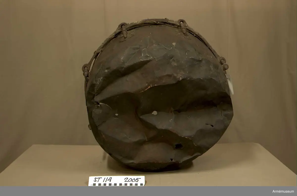 Tillstånd 2005:
Kittel: kraftigt bucklig och sprucken på flera ställen. En mängd stickmärken i storlek 1 cm. - 4 cm. Fot: saknas. Spännskinn: saknas, förutom en liten flik - hängandes över kanten in i pukan - likaså är skinnet lämnat längsmed kittelkanten fastsytt genom ett smalt läderband. Spännring: rostig. Spännskruv: 8 st. Skruvfästen: 8 st. Bärrem: saknas.