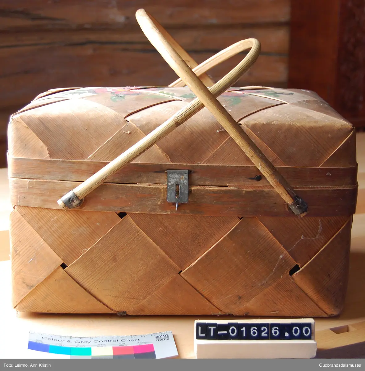 Rektangulær, flettet kurv av furu, håndtak av bambus, to håndtak samles til ett. Med låsemekanisme. Lokk festet til kurven med innslåtte metallkroker.