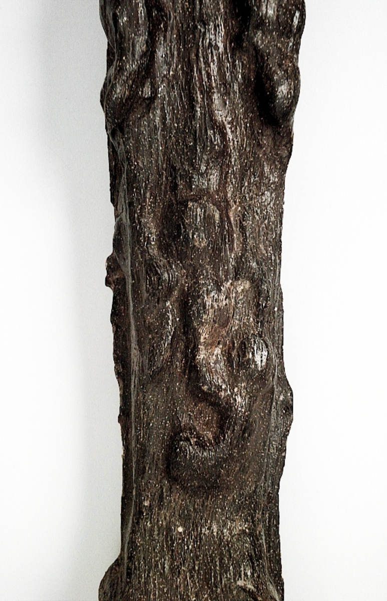 Skulpterad pilaster föreställande en herm eller möjligtvis en karyatid, under jonisk kapitäl.
Huvudet är vridet åt vänster samt prytt med en krona. Armarna hålls sträckta utefter sidorna.
Kroppen övergår i det med blad- och blomornamentik rikt sirade pilasterskaftet som smalnar av nedåt. Skaftet avgränsas genom en enkel vulst eller list från den rikt sirade och mjukt utbuktande piedestalen. Nedtill är piedestalen försedd med en bred bas. Skulpturens baksidan är slät.
Skulpturen är sliten.

Text in English: Sculptered pilaster with a Herm, or possibly a Caryatid, beneath an Ionic capital.
The head, with a crown, is turned to the left. The arms are streched out along the sides.
The body extends into the shaft of the pilaster, which tapers downwards and is richly decorated with leaf and flower ornamentation. A simple torus or batten separates the shaft from the richly decorated, softly bulging pedestal that has a broad base. The back of the sculpture is smooth.
The sculpture is worn.