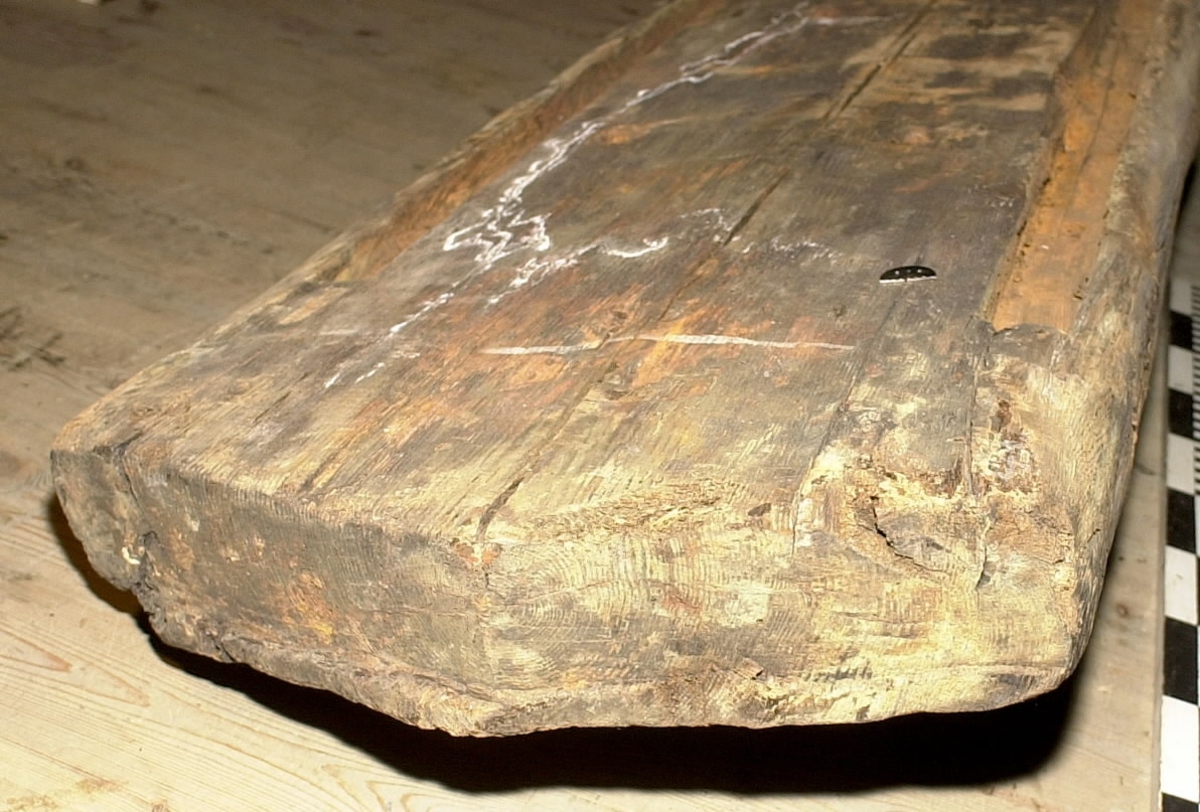 Mastkärna.
Kvadratiskt tvärsnitt. Avsågad/tillputsad i nedre delen efter bärgningen. Andra änden, toppen, är kilformad och spetsigt huggen med liten läpp längs ena sidan. 4 spår för mastjärn utmed långkanterna. Rostfläckar i spåren. Ett urtag på mitten av föremålet. Sprucken. Omkring 30 bulthål. Märkt med blå dymotejp.
Vriden efter bärgning.