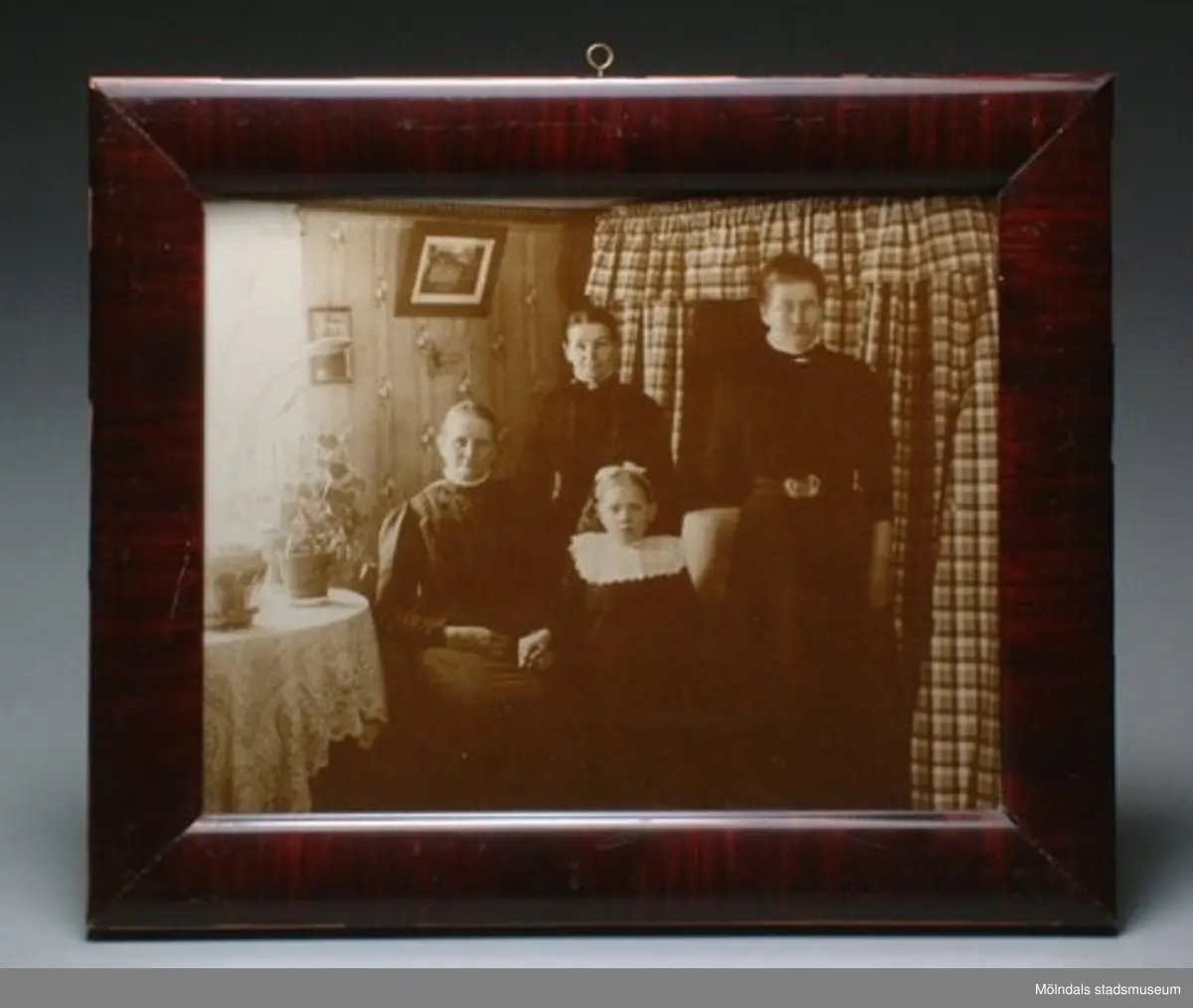 Från "Olas" i Våmmedal. 
Avporträtterade personer är Maria Eriksson, fosterflickan Märta, pigan Anna Carlsson och Fina (Josefina) Eriksson. Maria Eriksson är syster till Josefina.
Fosterflicka Märta Persson hade puckelrygg och var från Göteborg. Hon bodde en period hos systrarna Eriksson i "Olas". Som vuxen bodde hon i Sionkapellet i Kållered där hon var organist. Hon avled i Kållered.