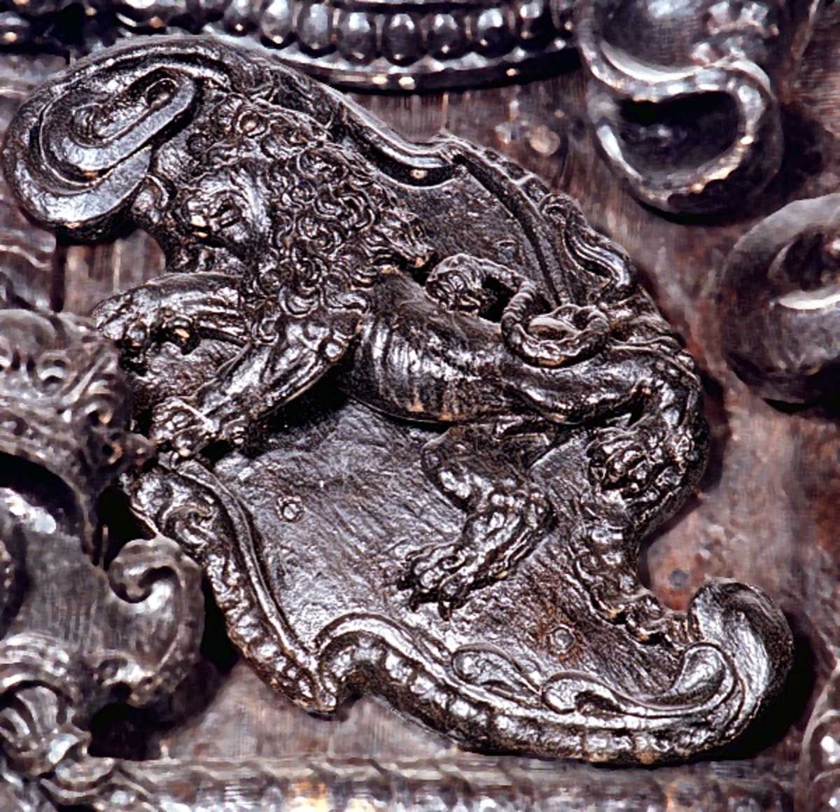Skulpterad sköld med upprätt, mot höger gående lejon. Lejonet är snidat i hög relief, med heraldiskt stiliserad hållning. Sköldens kontur är rokokomässig, med kanter av varierande bredd och rik pärlbroskdekoration. Upptill avslutas skölden med en ellipsformad broskvolut. Sköldens baksida är slät.

Text in English: Shield with upright, rightward-facing lion. The lion is carved in high relief and reproduced in perspective. It is seen in profile, and its posture is heraldically stylised. The shield has an almost rococo-like outline, with edges of varying width and rich earshell work decorations.The top is finished with an ellipse-shaped pearlwork scroll. The reverse side of the shield is smooth.