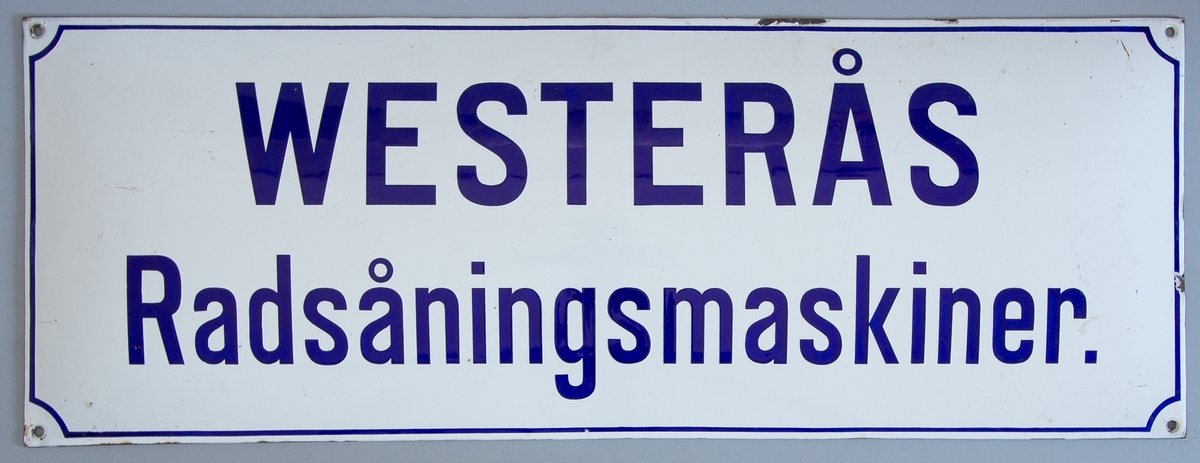 Reklamskylt i emaljerad plåt, rektangulär till formen. Vit botten med blå ram samt texten "WESTERÅS Radsåningsmaskiner.". Hål i hörnen för upphängning.