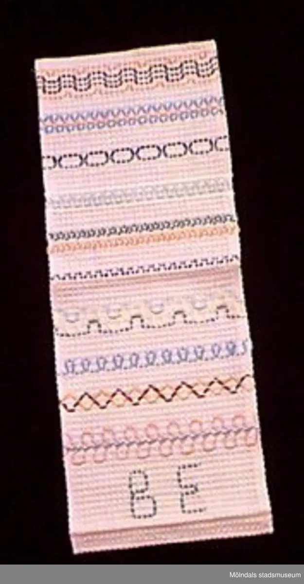 Ett stycke broderat rosa bomullstyg i våffelväv. Broderat i gröna, blå, rosa, gula och bruna färger. Olika dekorativa mönster utförda som provtekniker. Undervisningsmaterial för åk 3 och 4. Samhör med 02653-02661.Övriga uppgifter se 02643:1.