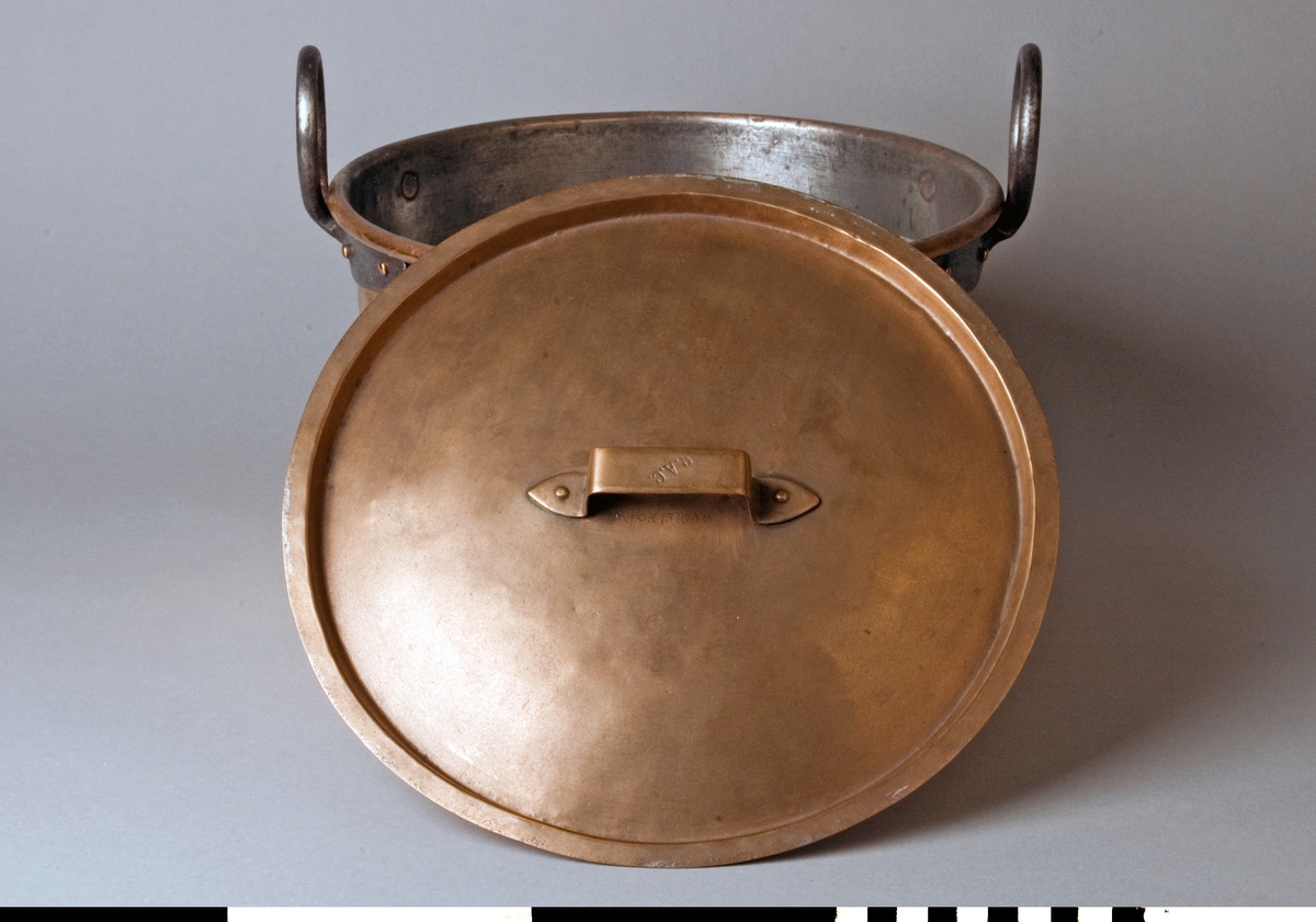 Gryta med lock tillverkad av koppar. Lock med bygelhandtag fäst med två nitar. Fals runt kanten. Märkning på bygeln: C.A.C. Locket är troligen av senare tillverkning. Grytan har en förtent insida. Lätt utåtlutande sidor, 167 mm höga. Överkanten är rullad utåt runt en stödtråd. Runda grepar av grov järntråd med utsmidda avlånga fästen, fyra rullade nitar till varje grep.