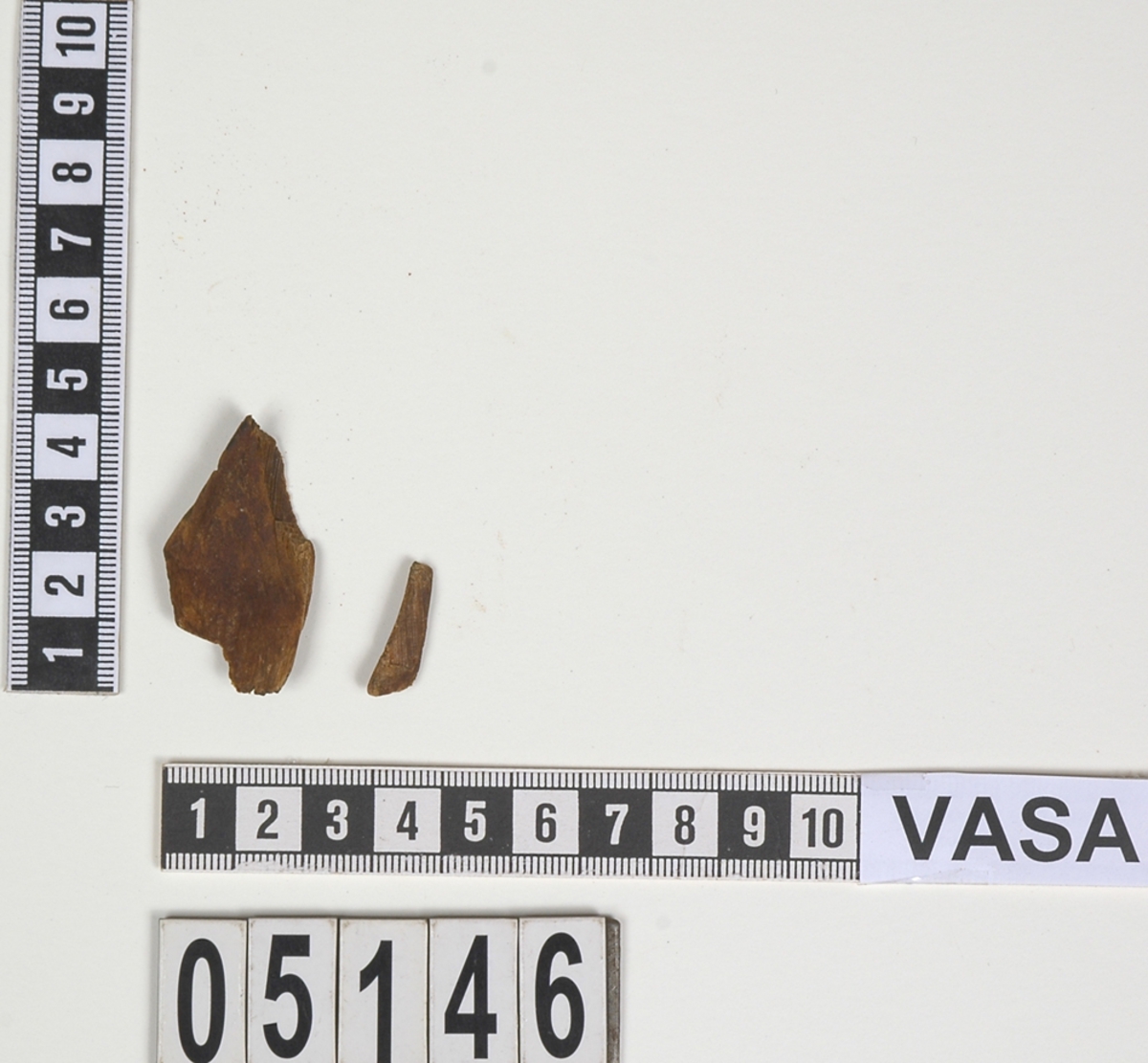 Delar av en träsked. Det finns en större del och ett mindre fragment av skedbladet. Den större delen har en något kupad form. På delarna syns en rödbrun färg, möjligen spår av bemålning.
Skeddelarna är mycket ömtåliga och i dåligt skick.