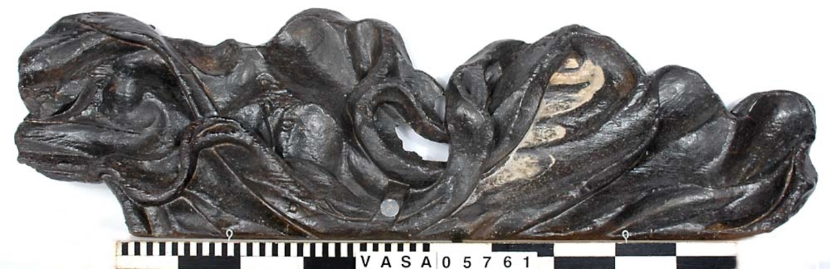 Del av skulptur. Mantel tillhörande Stora krigaren på babord sida. Skulpterat i ett stycke. I gott skick.