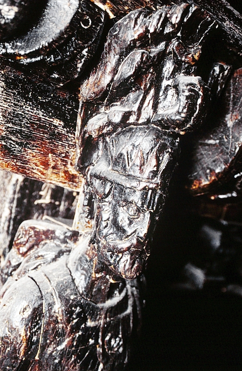 Skulptur föreställande en mansfigur med ett långsmalt och skäggigt ansikte, under en hög, slät hjälm med stora plymer. Runt hjälmen är en stålkrona trädd. Bakom huvudet skymtar ett snäckskal. Figuren är iförd en rikt ornerad rustning av thoraxmodell. Utefter figurens rygg hänger en mantel, som också draperar den vänstra axeln.

Hela figuren är frontalt framställd. Höger arm hålls lätt böjd utefter sidan, med handen fattande om ett svärdsfäste. Vänster arm är något böjd rakt ut från sidan, och handen verkar fatta tag om manteln. Kroppstyngden är jämnt fördelad på båda benen.

Figuren står på en sockel, vilken pryds av en bred och grimaserande maskaron. Sockeln är även försedd med en banderoll som tycks helt slät och utan namninskription.

Upptill är bakstycket framdraget i en kraftig "huvudplatta". Skulpturens baksida uppvisar tre snedställda, olika djupt liggande fält. Fälten, som utgör anliggningsytor, ger skulpturen en trappstegsformad profil.
Huvudplattan är delvis skadad. Svärdets klinga saknas. I övrigt är skulpturen relativt välbevarad.

Text in English: A sculpture representing a male figure with a long and narrow face that is bearded and has a moustache. On the head there is a plumed helmet on which a crown with points has been placed and behind the head a large sea shell. The figure is wearing richly decorated thorax type armour. The mantle is hanging down the back and draped over the left shoulder.

The figure faces towards the front. The right arm is slightly bent and held at the side and the hand holds a sword hilt. The left arm is slightly bent and held out from the side and the left hand seems to hold the mantle. The weight of the body is carried on both legs.

The figure stands on a plinth with a broad and grimacing mask and also has a label which is quite smooth and without any inscription.

The upper part of the back extends obliquely upwards in a powerful "head board". The sculpture''s back has three obliquely placed surfaces of different depths that are areas of attachment. The surfaces make the sculpture look like a step-ladder in profile.
The board behind the head is partly damaged and the blade of the sword is missing but otherwise, the sculpture is rather well preserved.