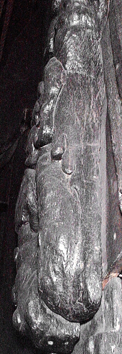 Skulptur föreställande en triton, svängd mot vänster och framställd i höger profil.
Tritonen har skäggigt ansikte, stor näsa samt en bladsmyckad hjälm på huvudet. Armarna är ersatta av långa, flikiga bladslingor. Bålens övergång i den fjällförsedda fiskstjärten markeras av stora bladbildningar. Figuren avtecknar sig i hög relief mot det släta bakstycket. Nedtill ses en fiskliknande stjärt med drakfena, vilken är fortsättningen på en under liggande draken, se fyndnummer 00628. På baksidan finns urtag för relingslisten.
Skulpturen är välbevarad.

Text in English: A sculpture of a Triton curved to the left, in right profile.
Bearded face with a long nose. Leaf-decorated helmet. The arms are replaced by long, lobed leaf formations. The transition between the male torso and the scaled fish-tail is decorated with large leaves. The figure is seen in high relief against a plain back board. Below the figure can be seen a section of another fish-like tail but actually a dragon''s fin, belonging to the dragon situated underneath, see No. 00628. There are notches on the back of the sculpture that fit into the railing.
The sculpture is well preserved.